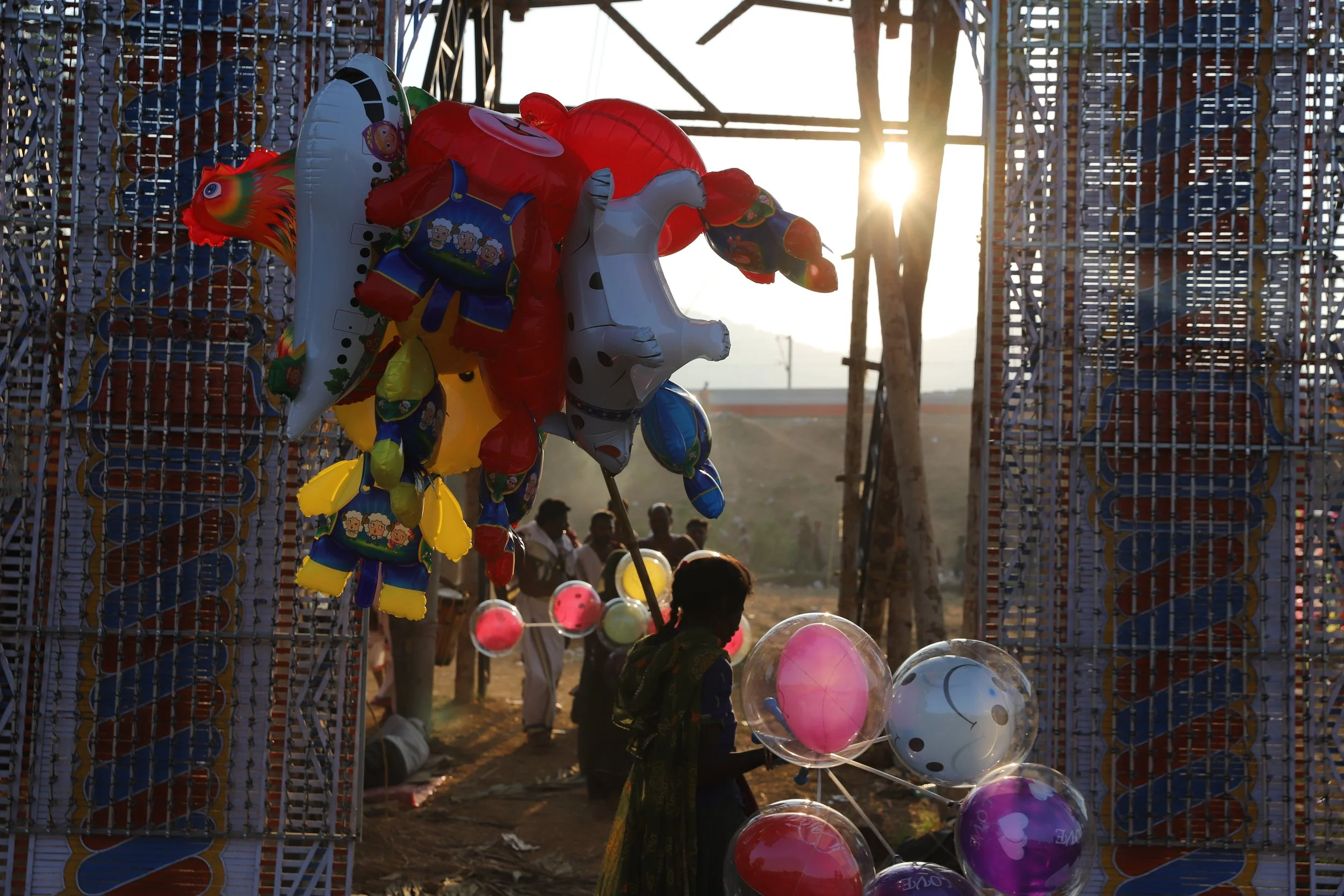Children at a fairground at sunset with colorful balloons and game stalls.