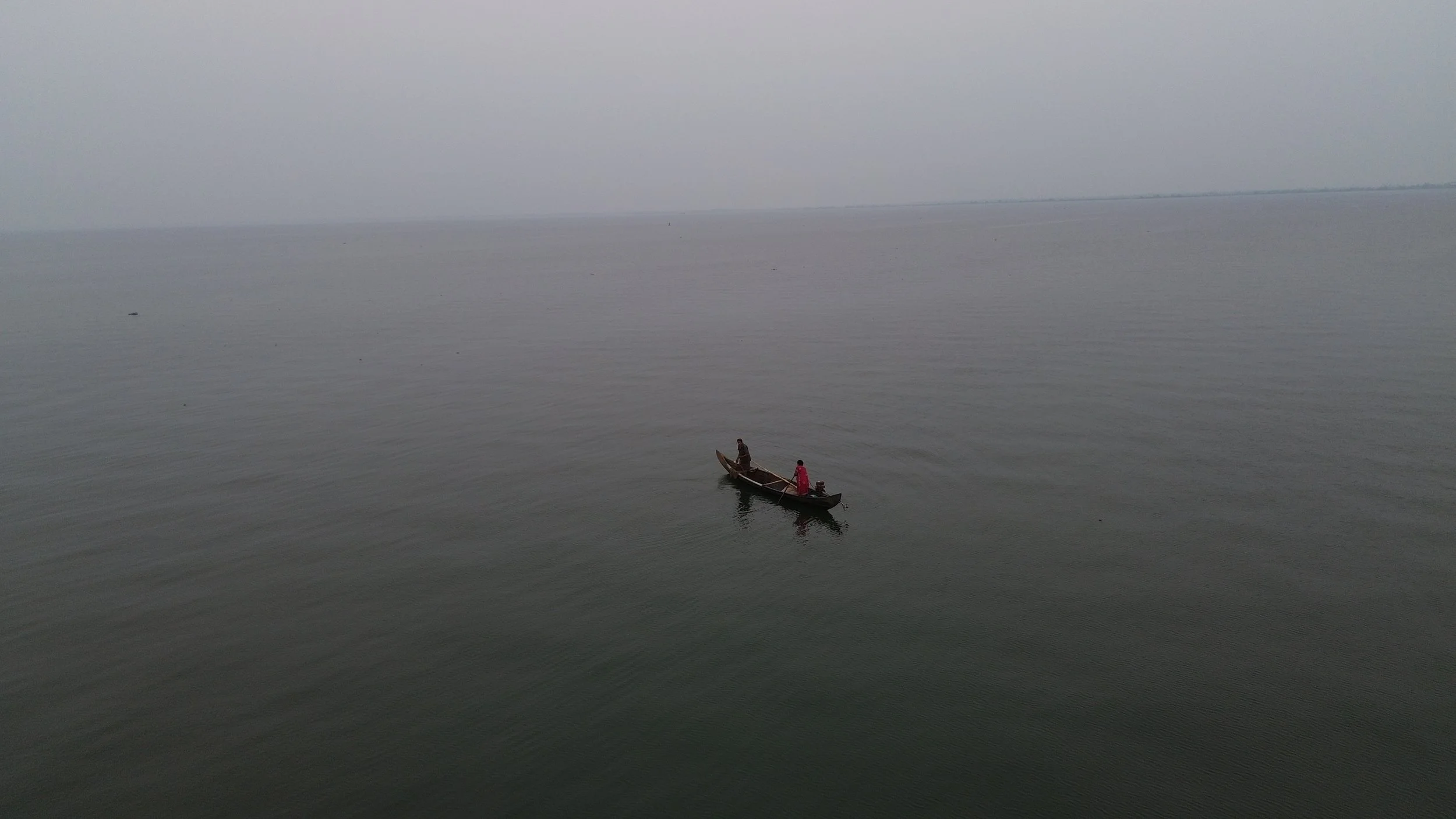 A small boat with two people rowing on calm water under a cloudy sky.