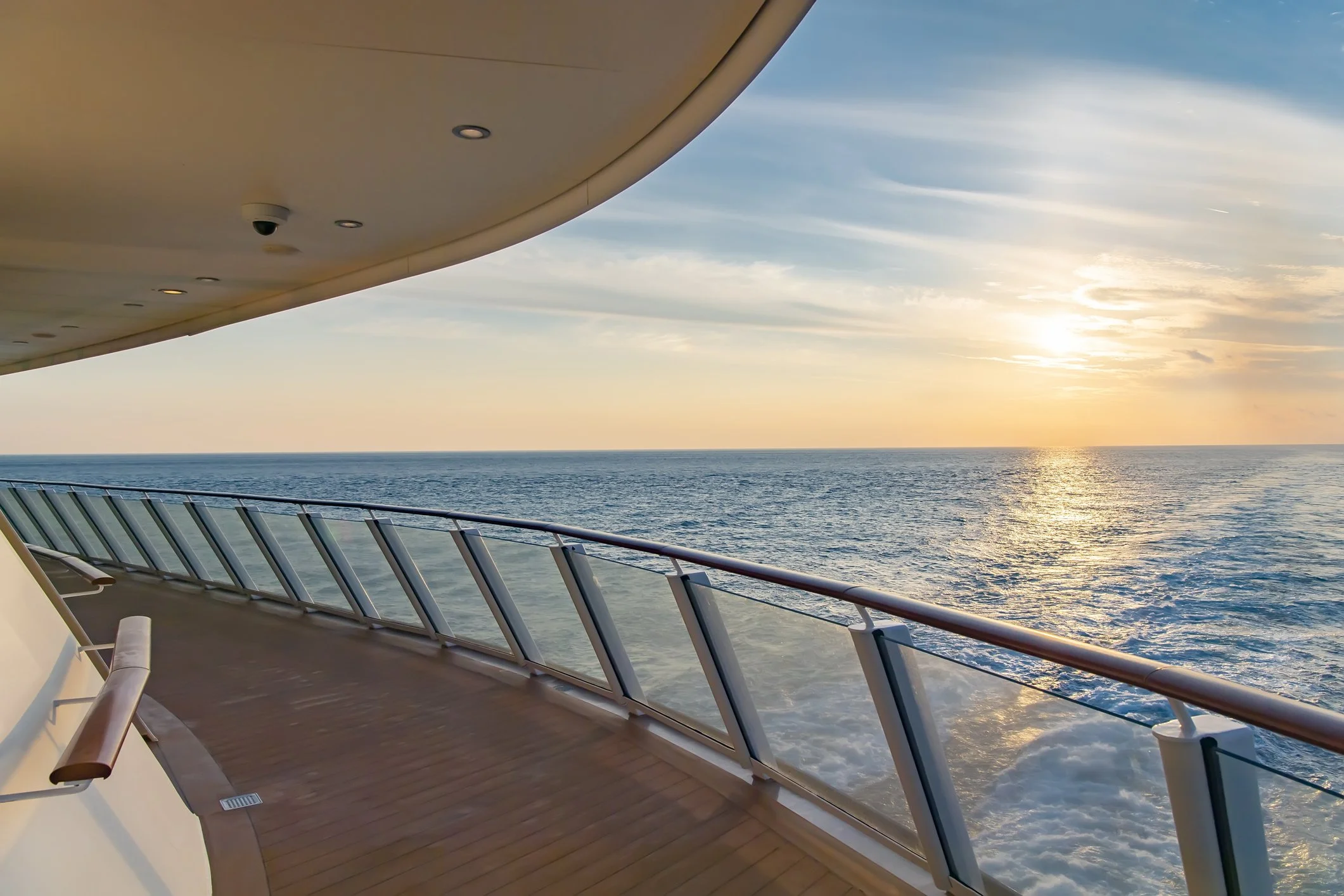 View of the ocean at sunset from the deck of a cruise ship, with a curved ceiling and glass railing.