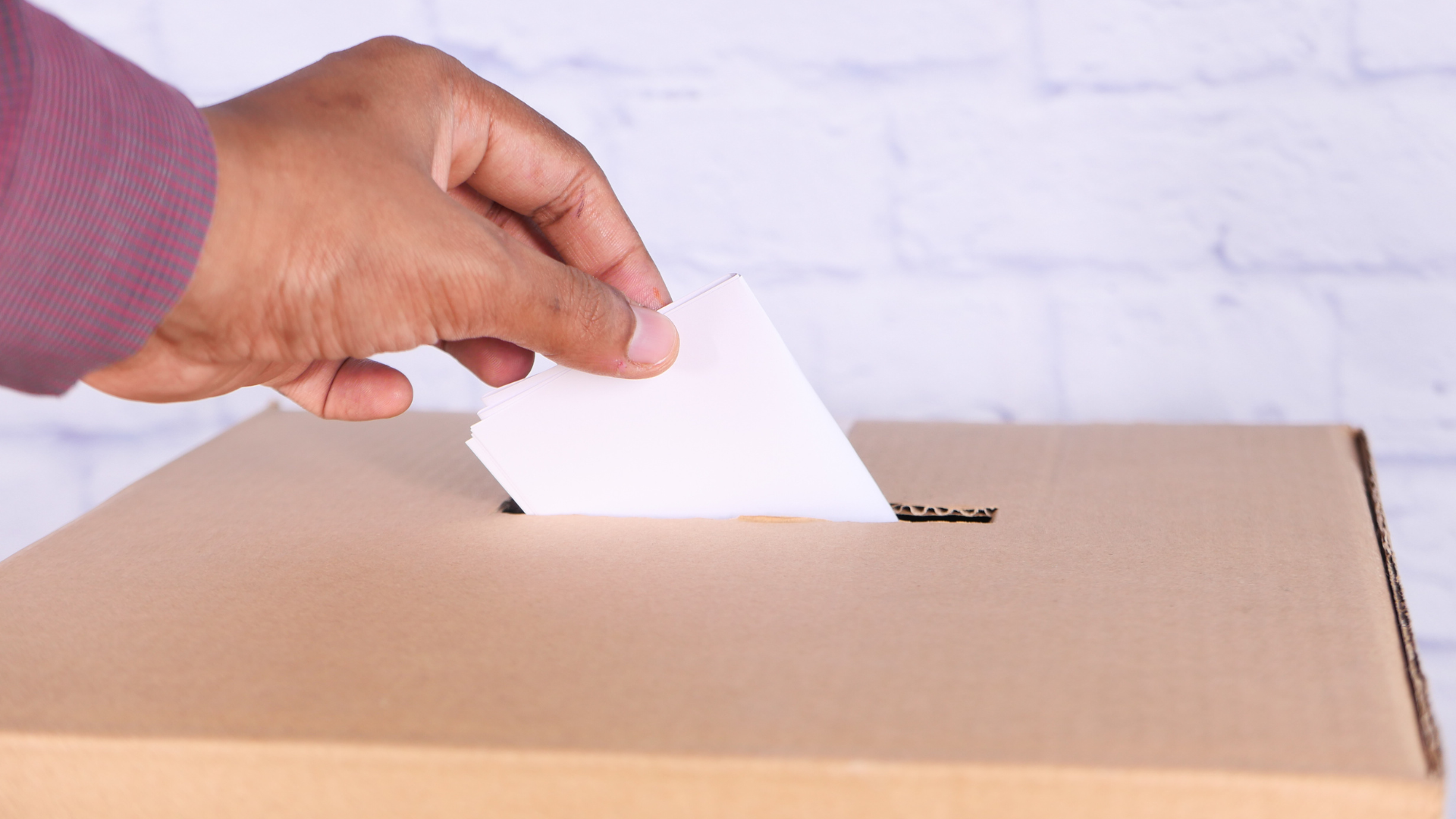 Person placing a ballot into a cardboard ballot box for voting