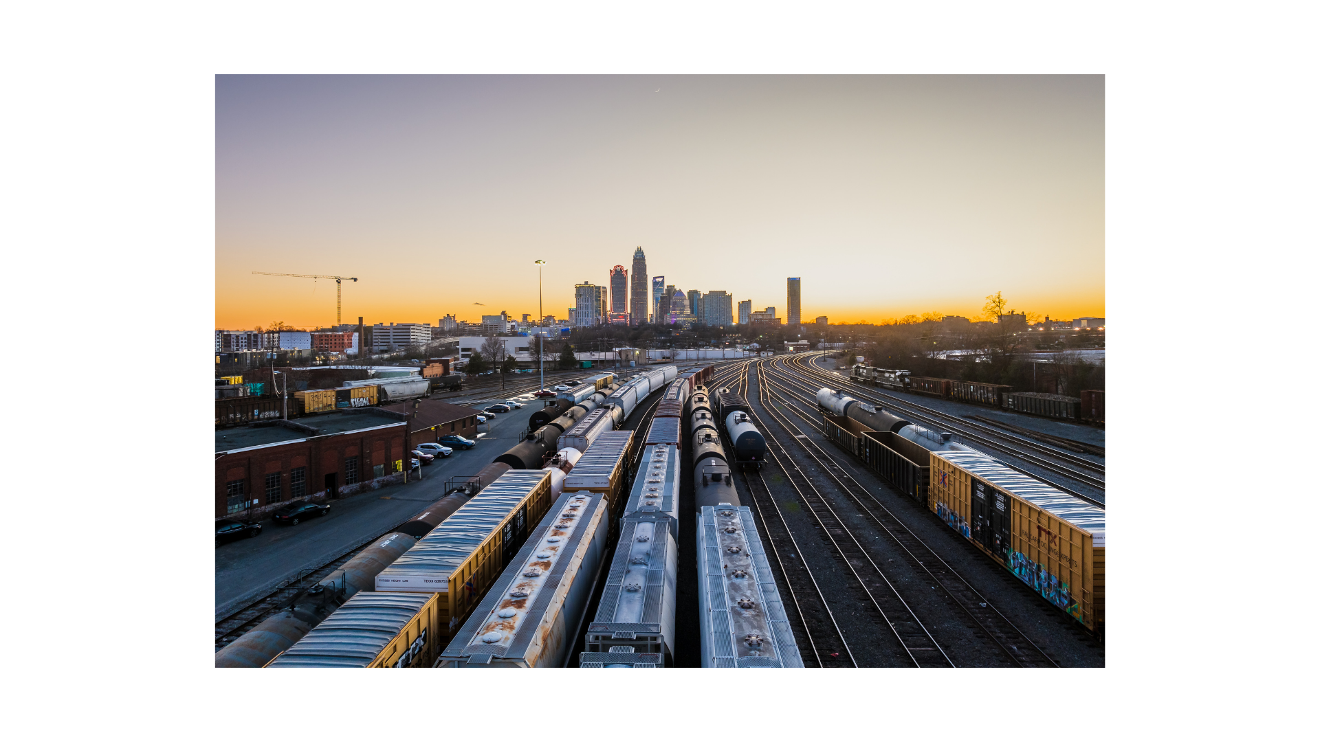 City of Charlotte skyline at sunset with train tracks and freight trains in the foreground.