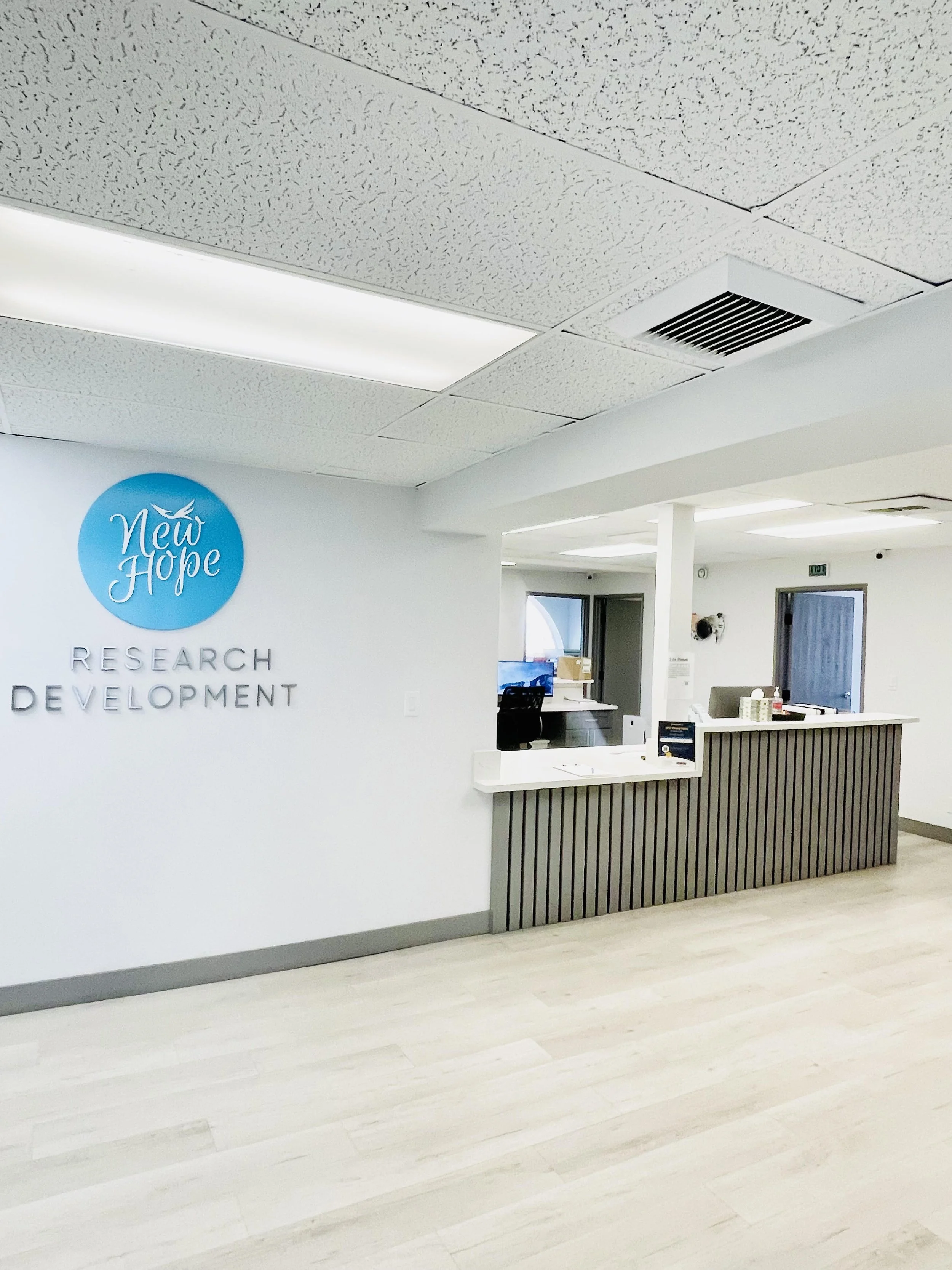 Reception area at New Hope Research and Development with a blue circle logo and a white dove, white wall, modern reception desk, and a bright, clean environment.