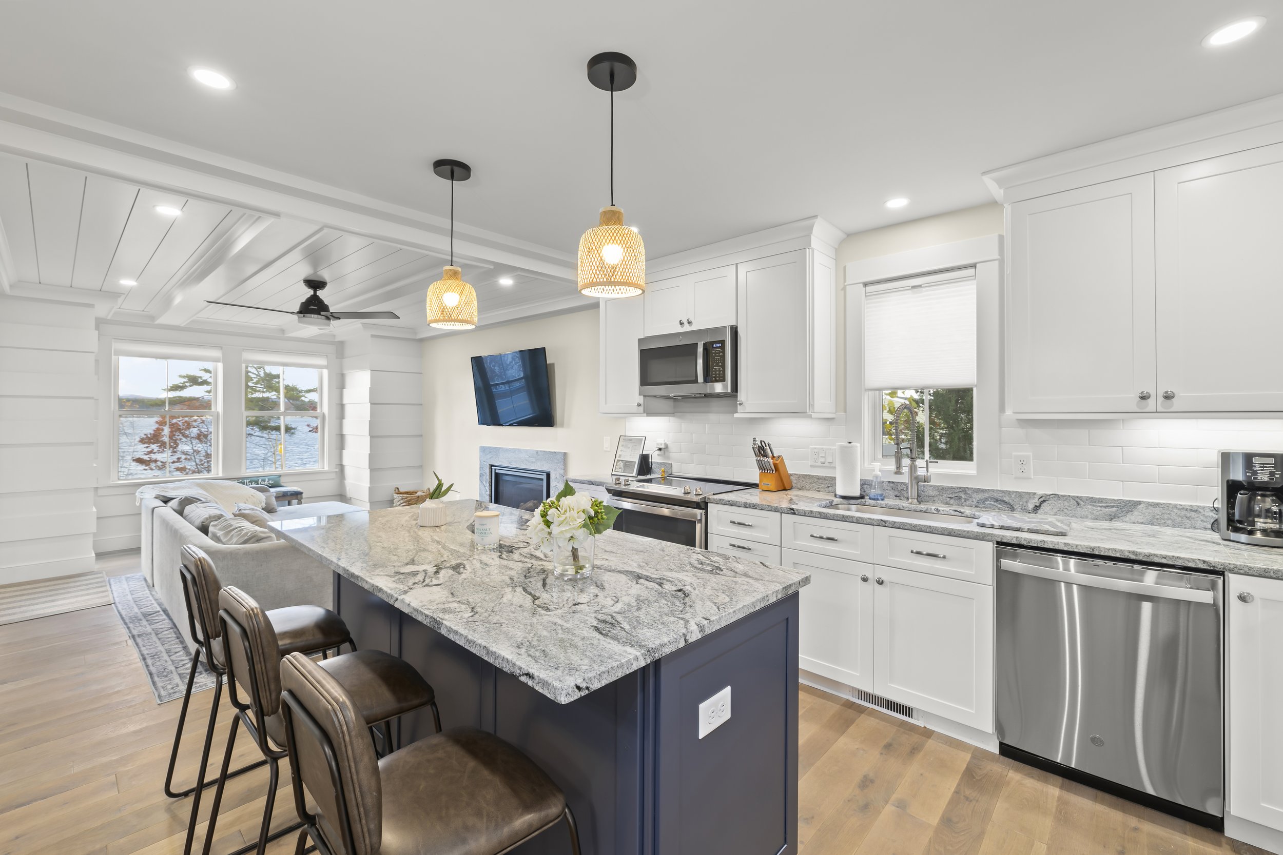 Kitchen with white cabinets, granite countertops, stainless steel appliances, island with four brown stools, window view of trees and water, and modern decor.
