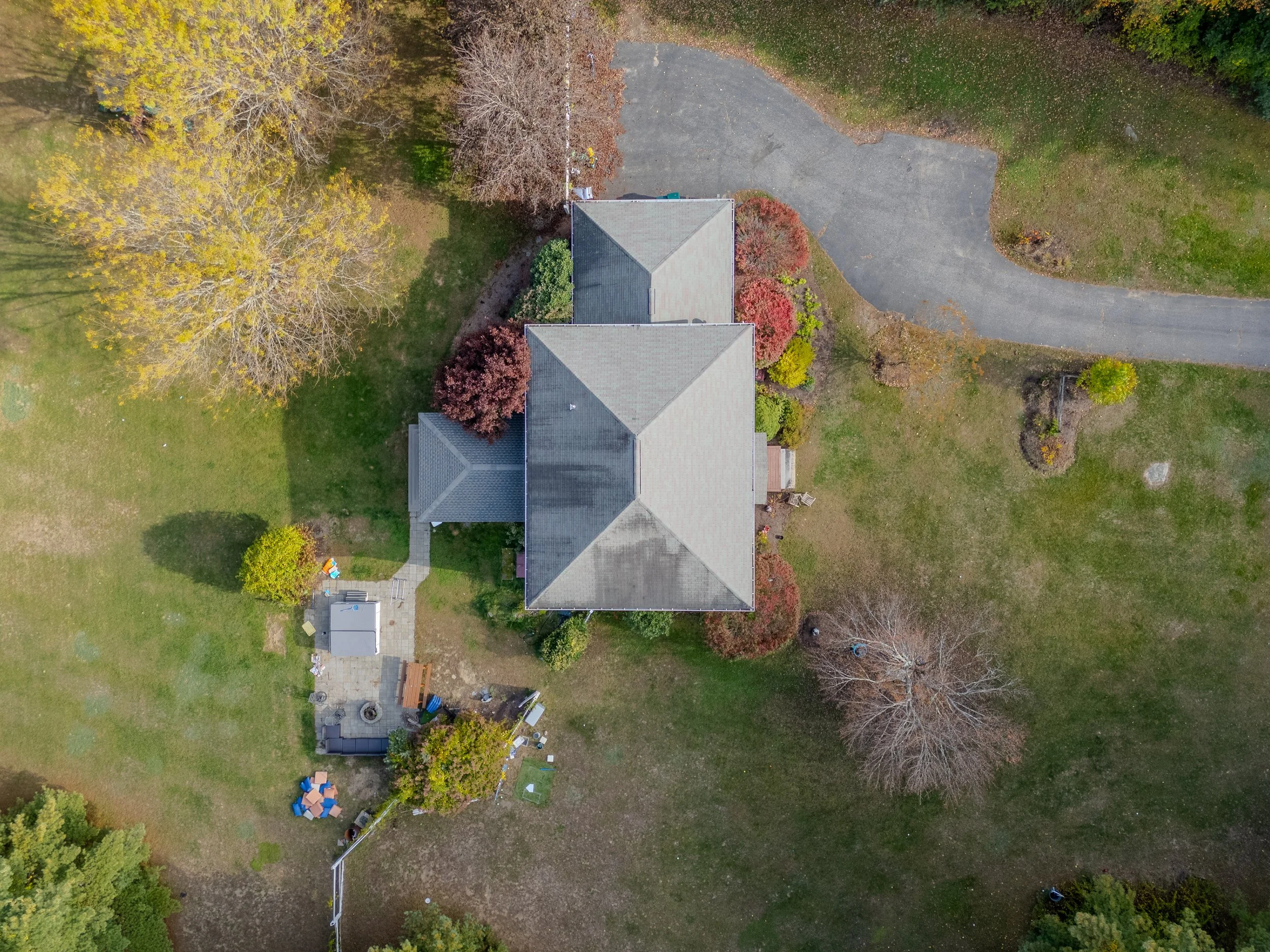 Aerial view of a house surrounded by yard, trees, and a driveway in a suburban area.