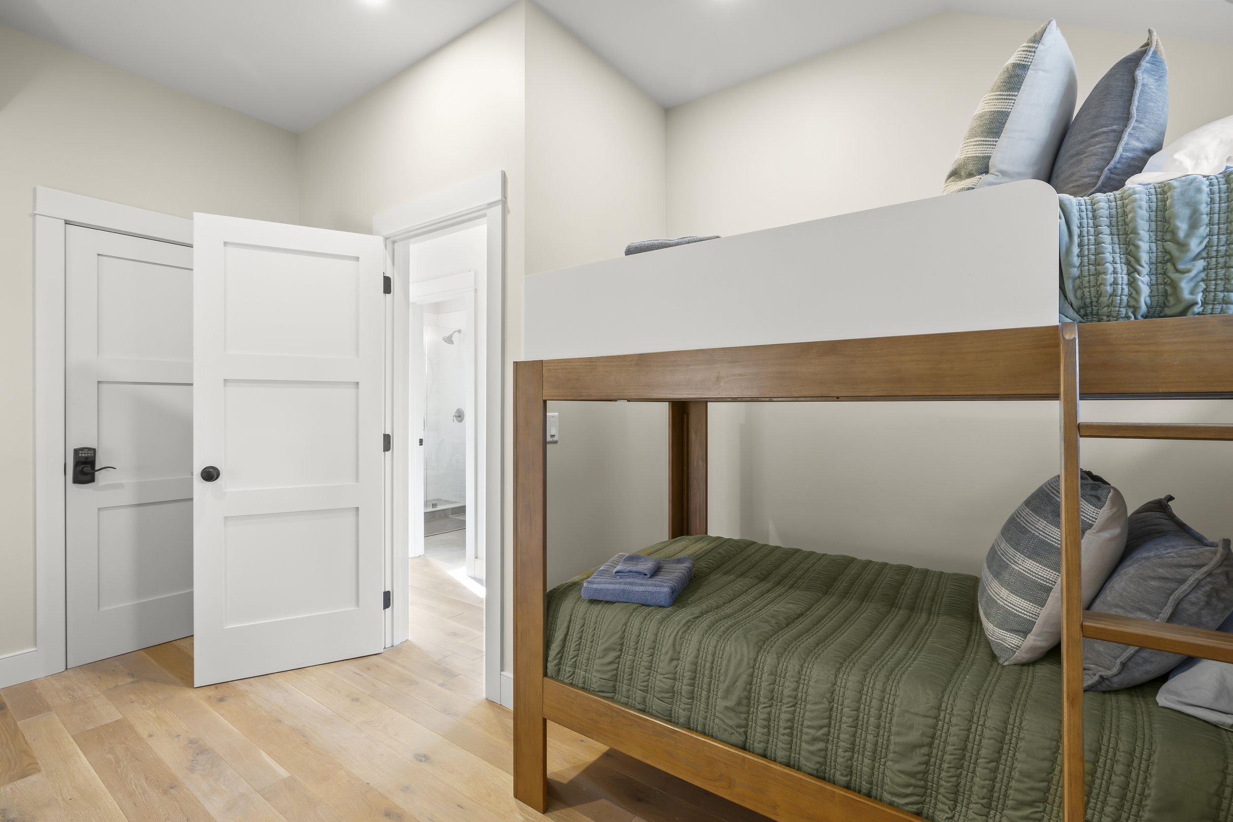 A bedroom with white doors, a bunk bed with a green bedspread, and a smaller top bunk with pillows, in a well-lit space.