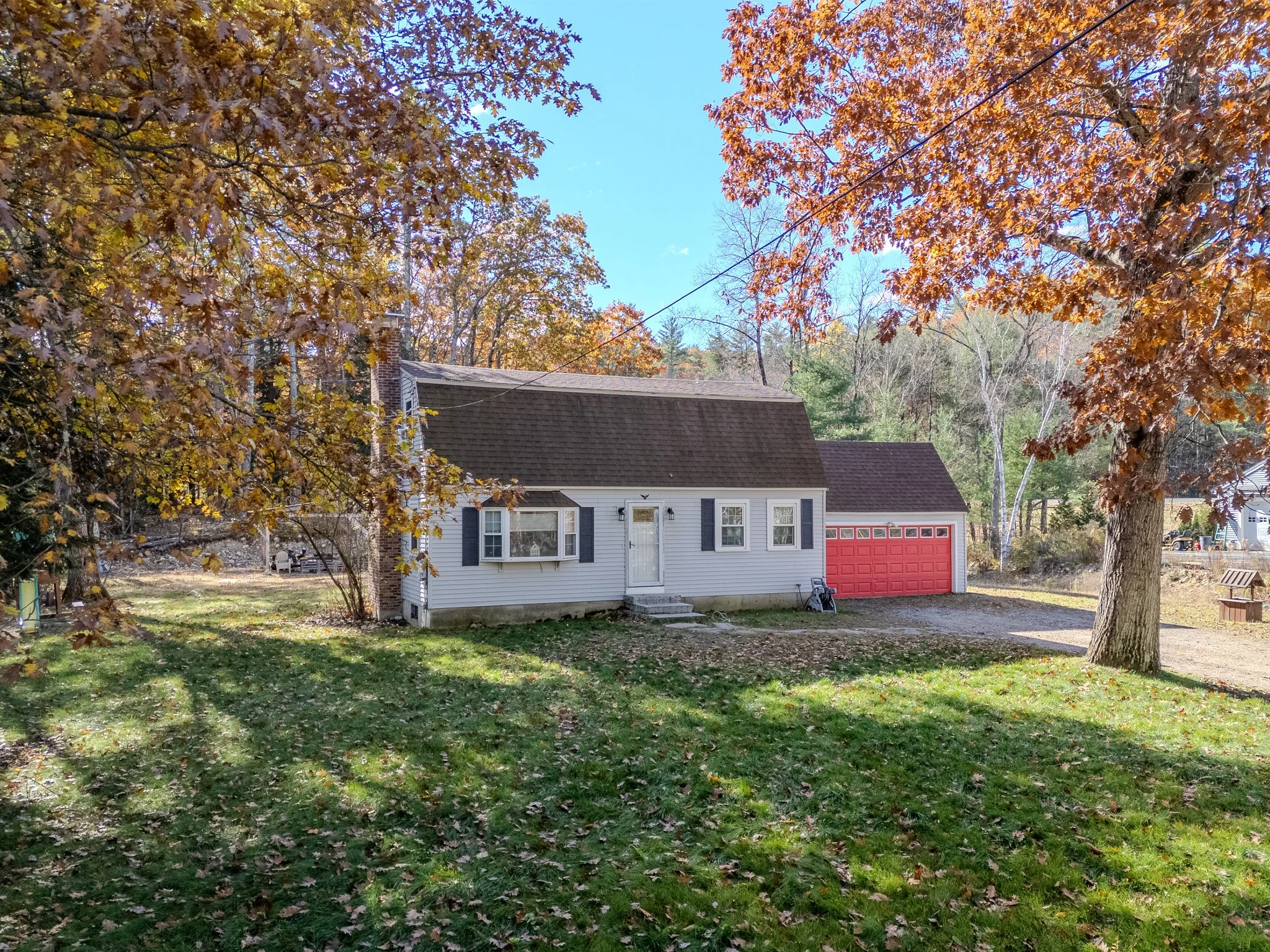 A house with white siding and a red garage door, surrounded by trees with autumn-colored leaves and a grassy yard.