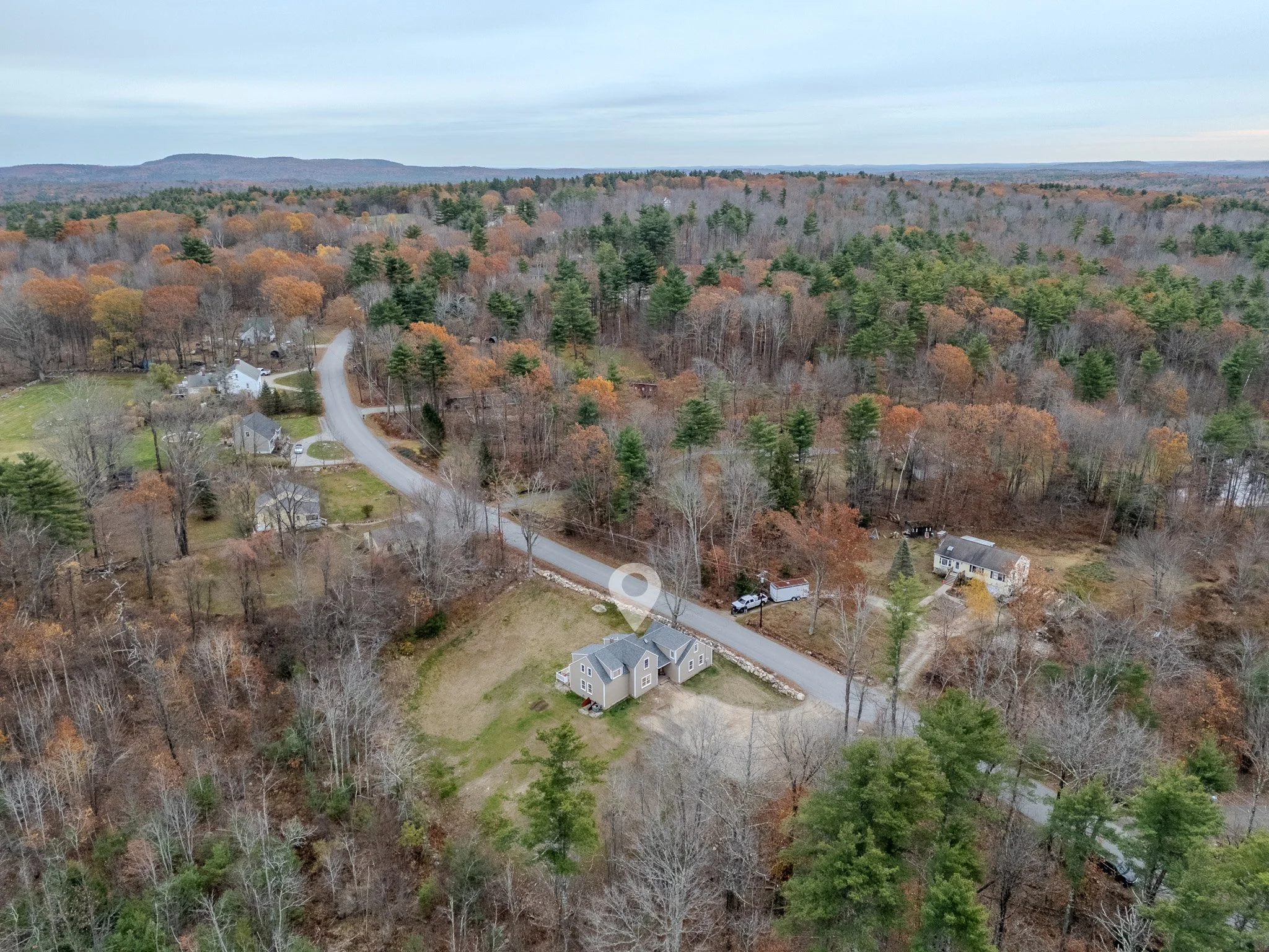 Aerial view of a rural neighborhood with houses, trees, and a winding road in a fall landscape.