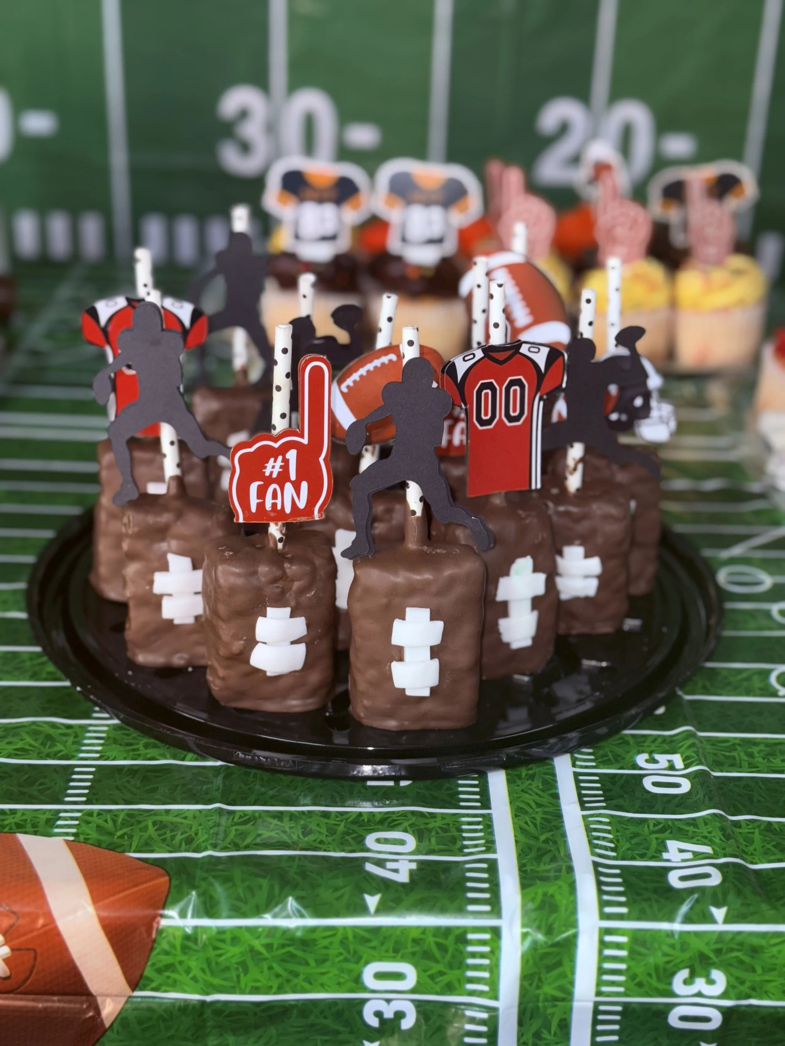 Football-themed chocolate cake with football and sports player decorations on a green football field tablecloth.