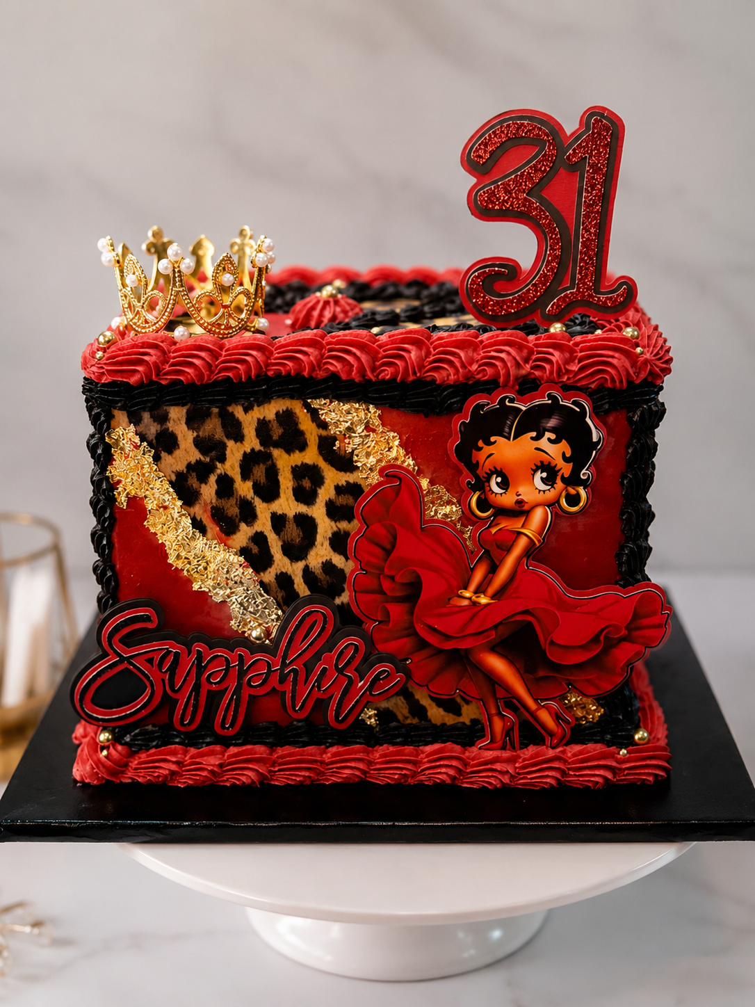 A red and black birthday cake with leopard print, a princess figurine, a gold crown, and a red number 31 topper, decorated with gold accents and red frosting.
