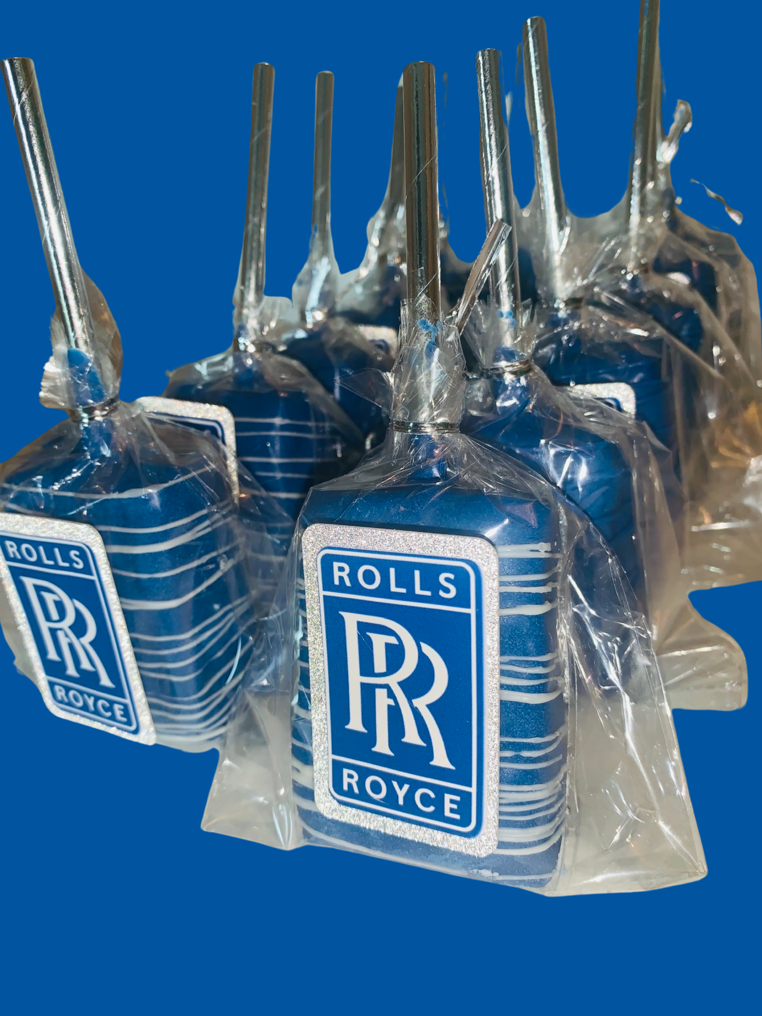 Close-up of multiple small packaged items with Rolls Royce branding, wrapped in clear plastic and arranged on a blue background.