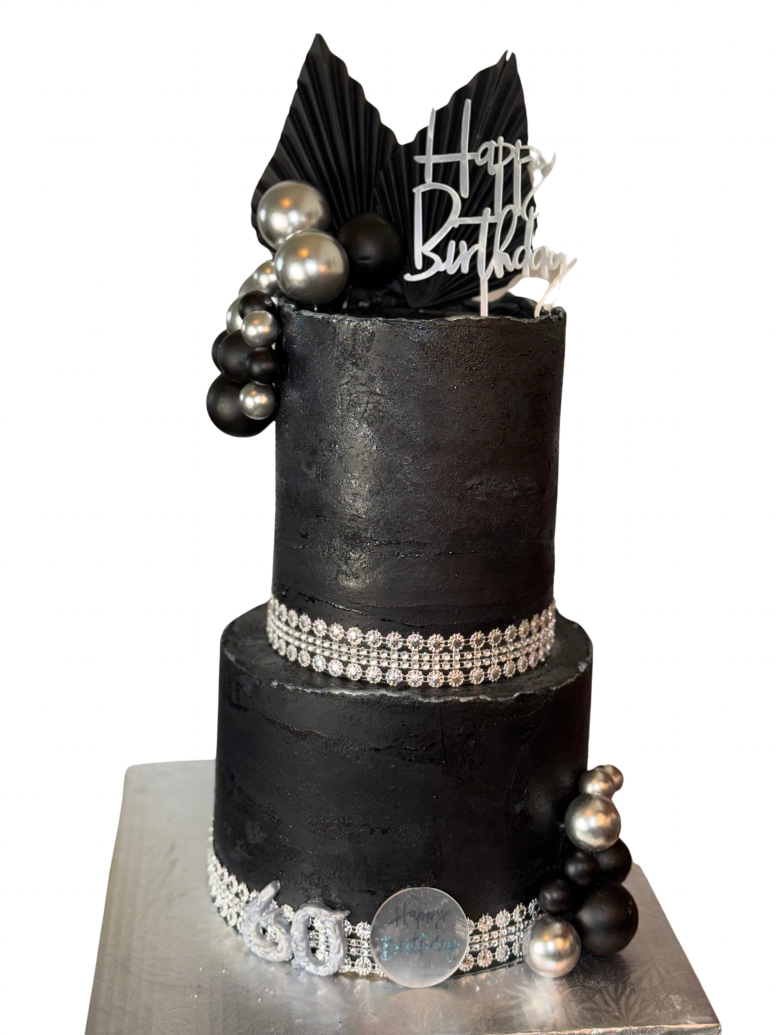 A two-tier black birthday cake decorated with metallic silver and black spheres, rhinestone bands, a 'Happy Birthday' topper, and the number '60' on the base.