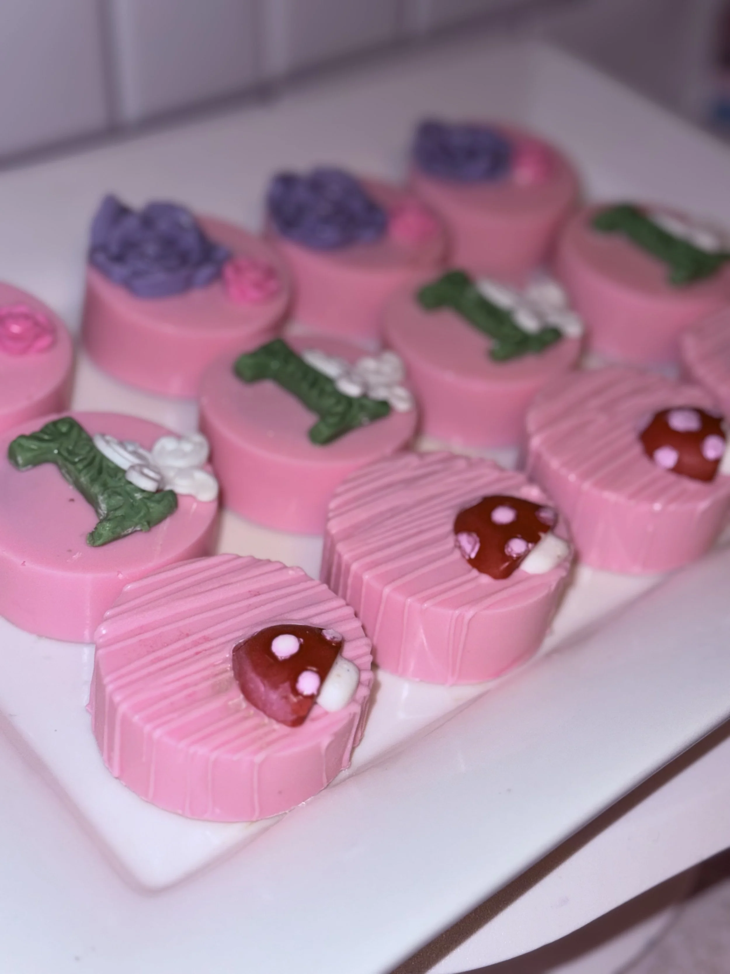 Plate of pink and purple Valentines Day-themed chocolates with decorative flowers, hearts, and alphabet 'I' letters.