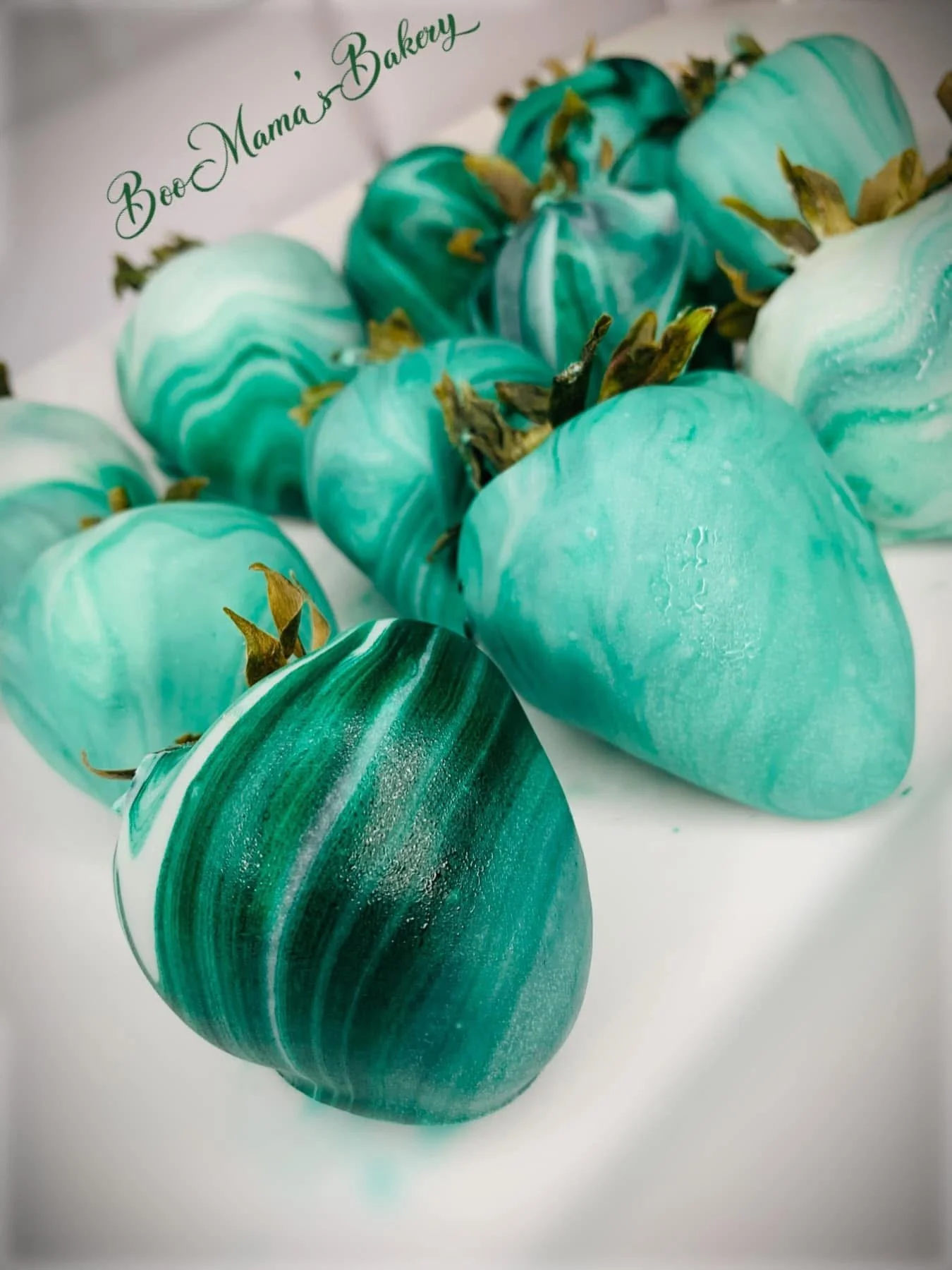 Multiple turquoise and green marbled strawberries with brown leafy stems on a white background.