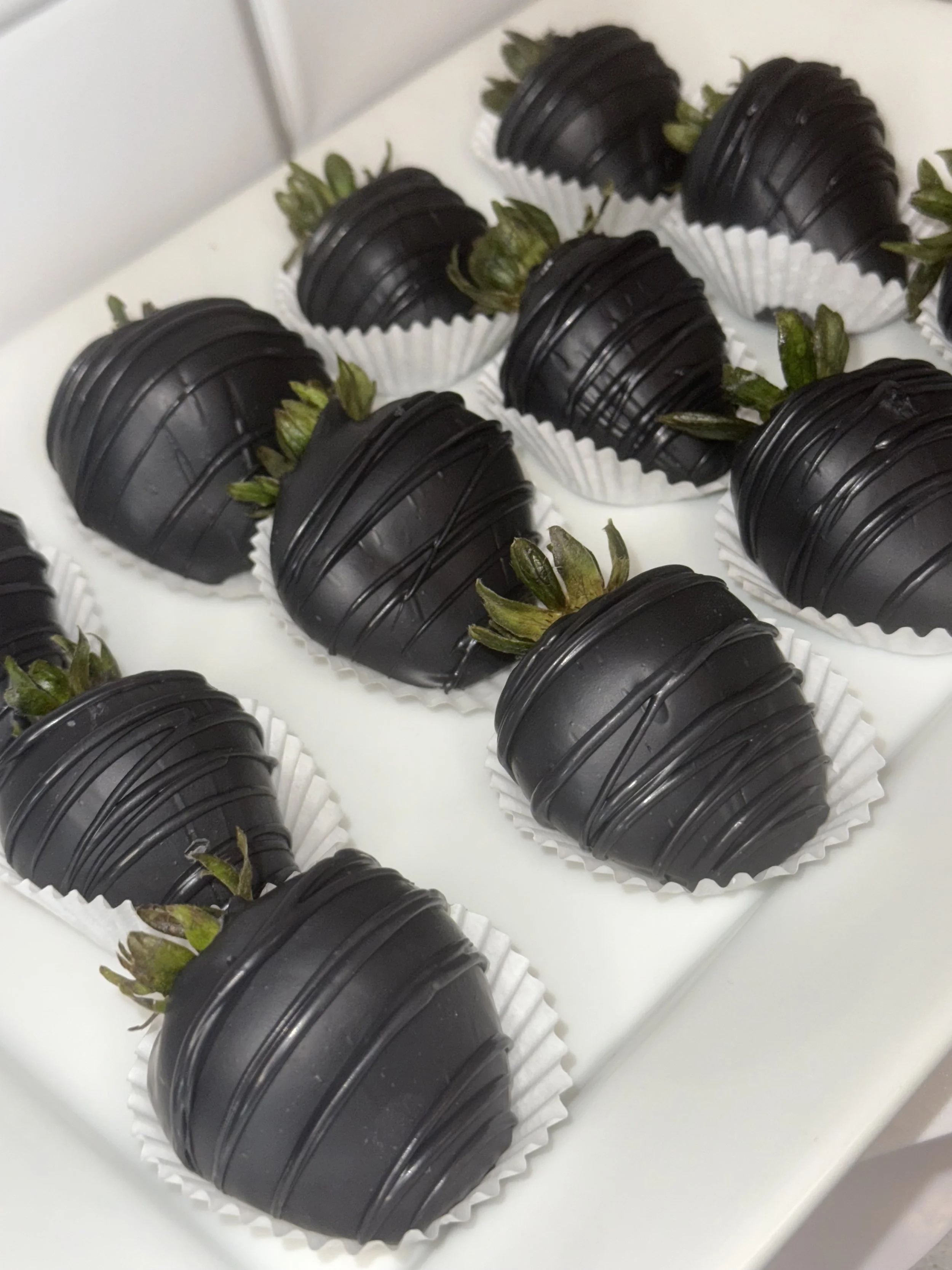 Chocolate-covered strawberries arranged in a white box, each placed in a white paper cup.