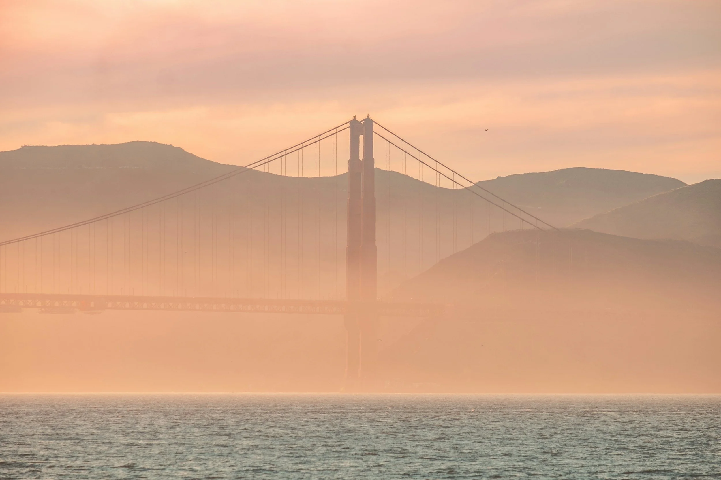 adult-residential-facility | Golden Gate Bridge shrouded in fog at sunrise or sunset with hills in the background and water in the foreground.