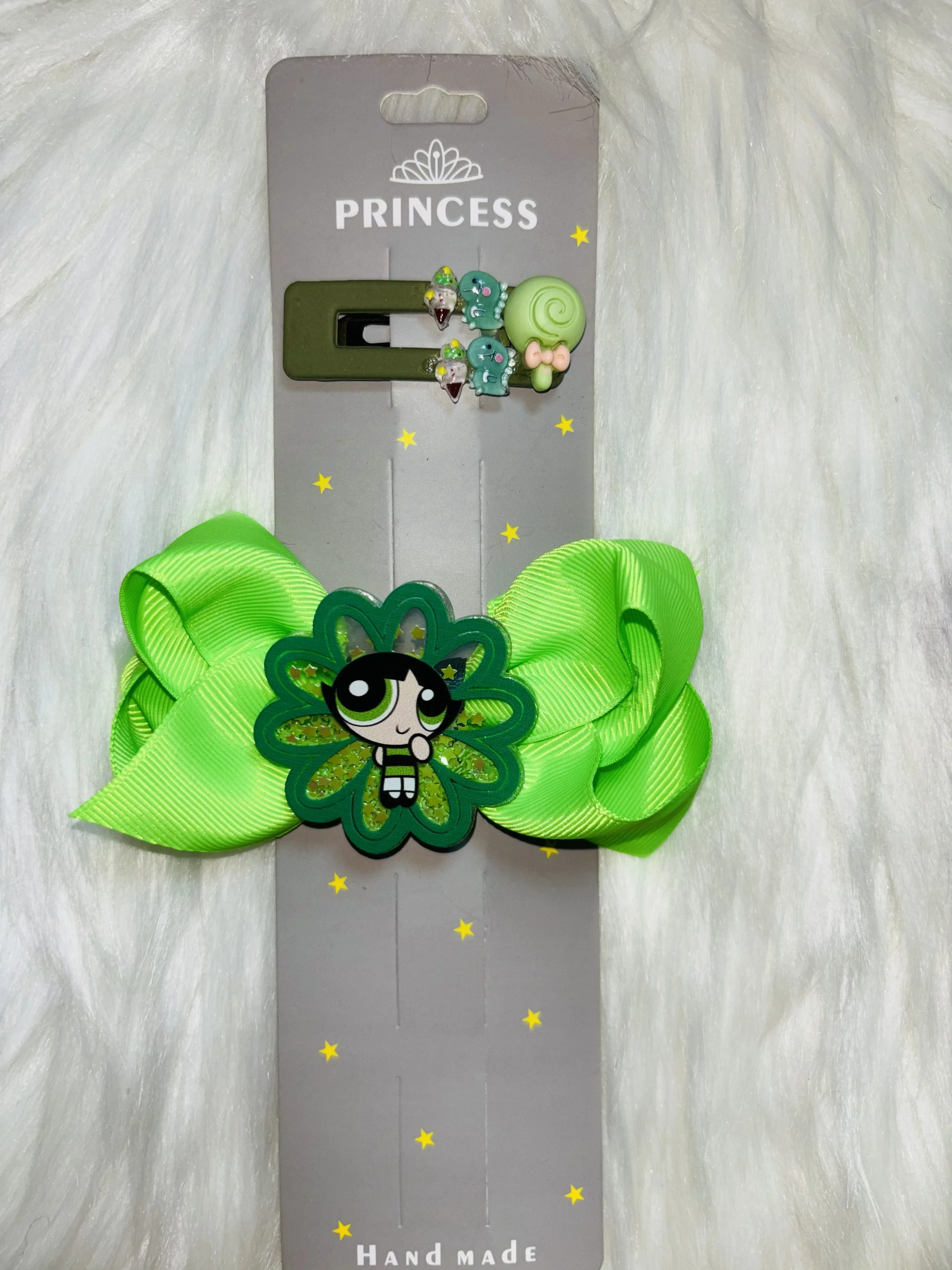 A handmade hair accessory with a large green bow, a charm featuring a cartoon girl with black hair and green eyes, star-shaped confetti, and a green traffic light clip, attached to gray backing card labeled 'PRINCESS' at the top and 'HAND MADE' at the bottom.