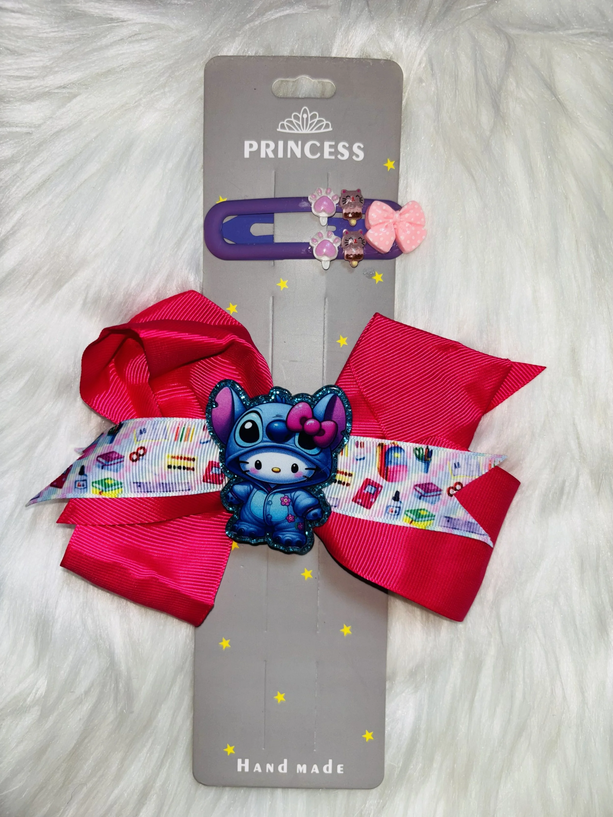 A handmade hair accessory featuring a large pink polka dot bow on a purple clip, attached to a decorative tag with the word 'PRINCESS', small yellow stars, and a cartoon character with blue fur and pink accessories.