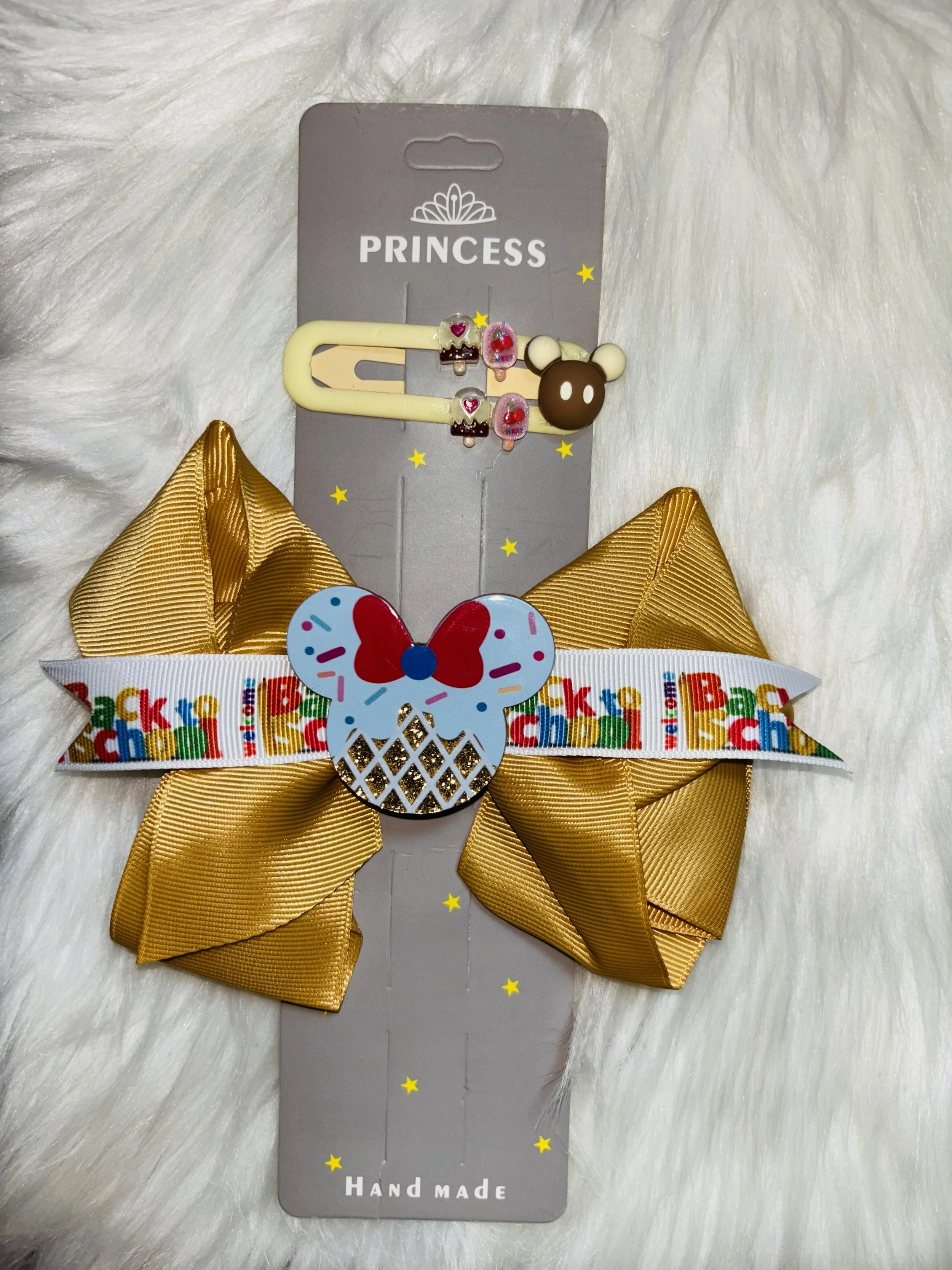 A decorative hair clip with a cream-colored base, featuring a bear face with cream ears, and small embellishments of cupcakes and ice creams, attached to a gray card with yellow star accents and the words 'PRINCESS' and 'HAND MADE'.