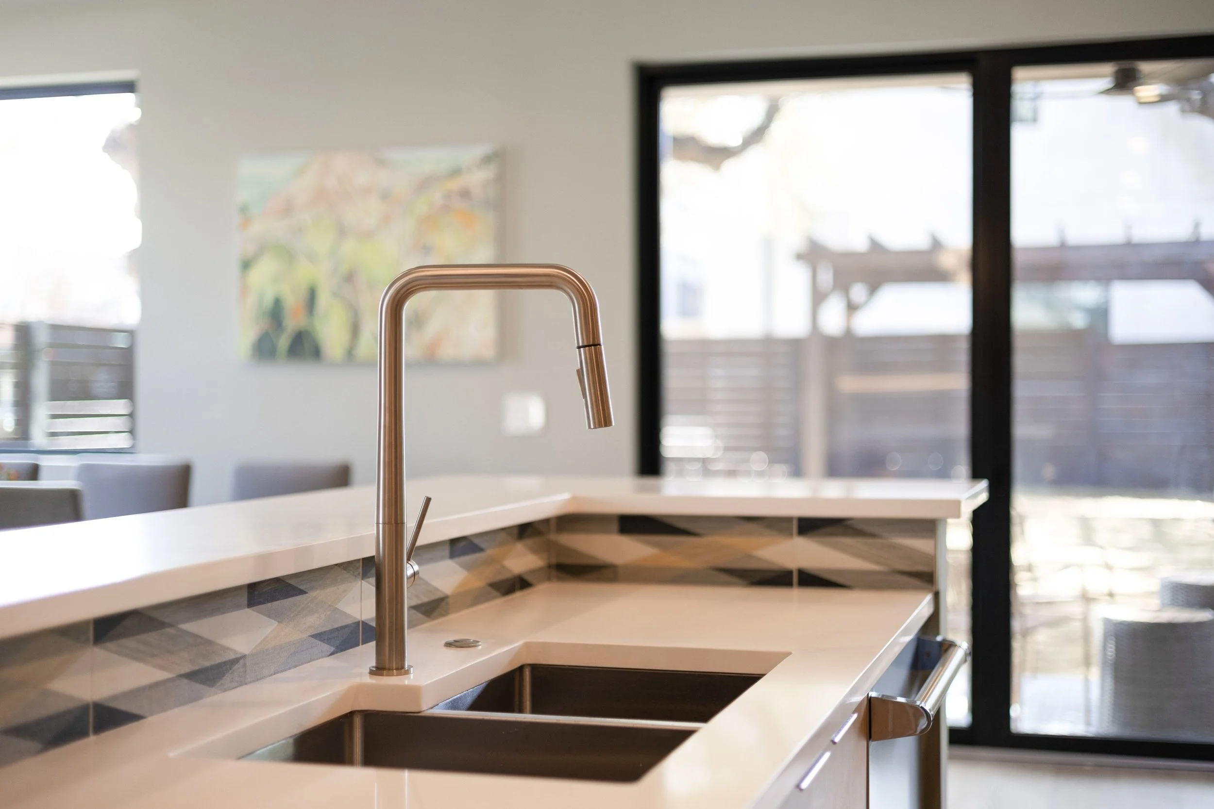 Modern kitchen with double sink, stainless steel faucet, and sliding glass door leading outside.
