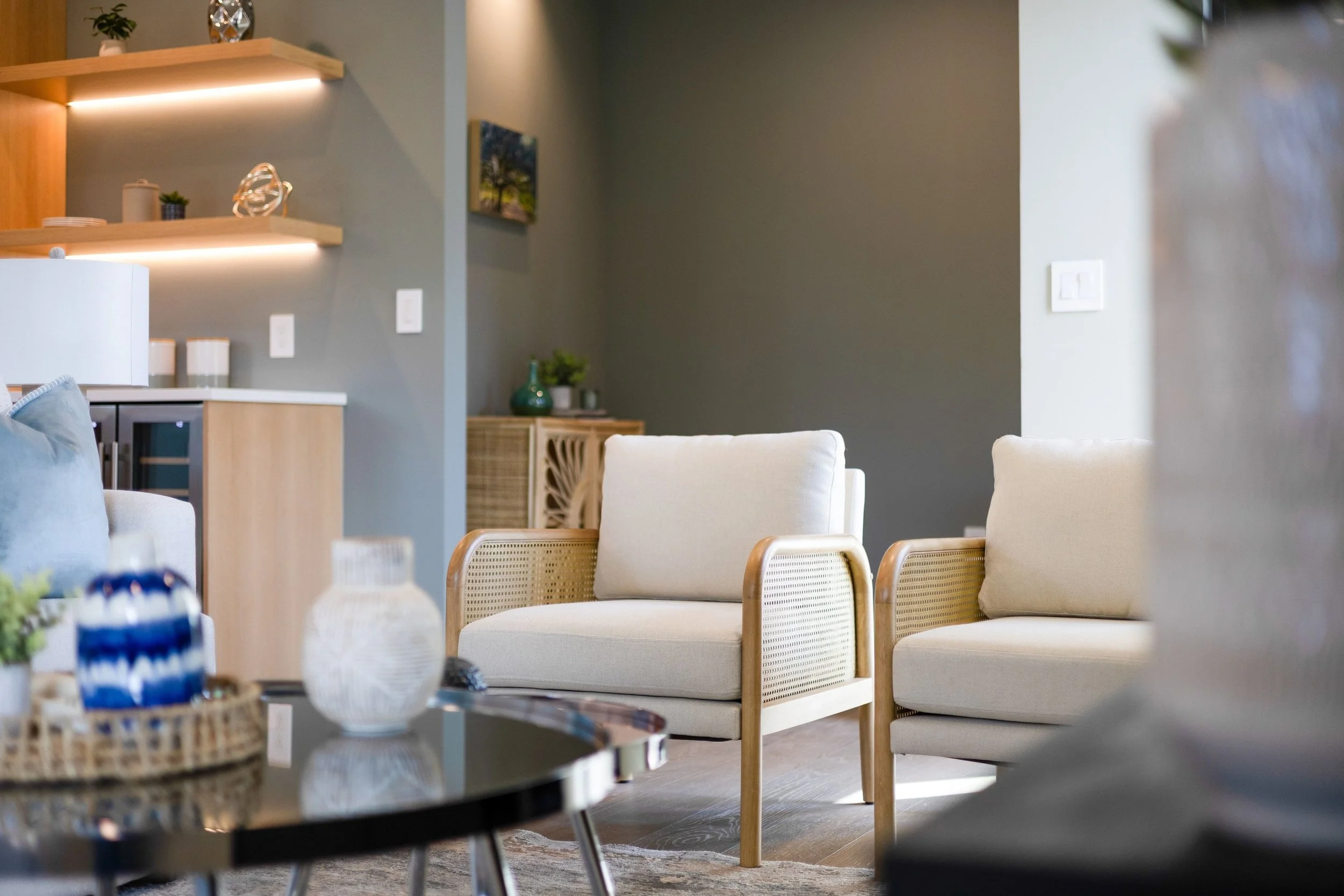 Living room with white armchairs, a coffee table, and decorative items on shelves.