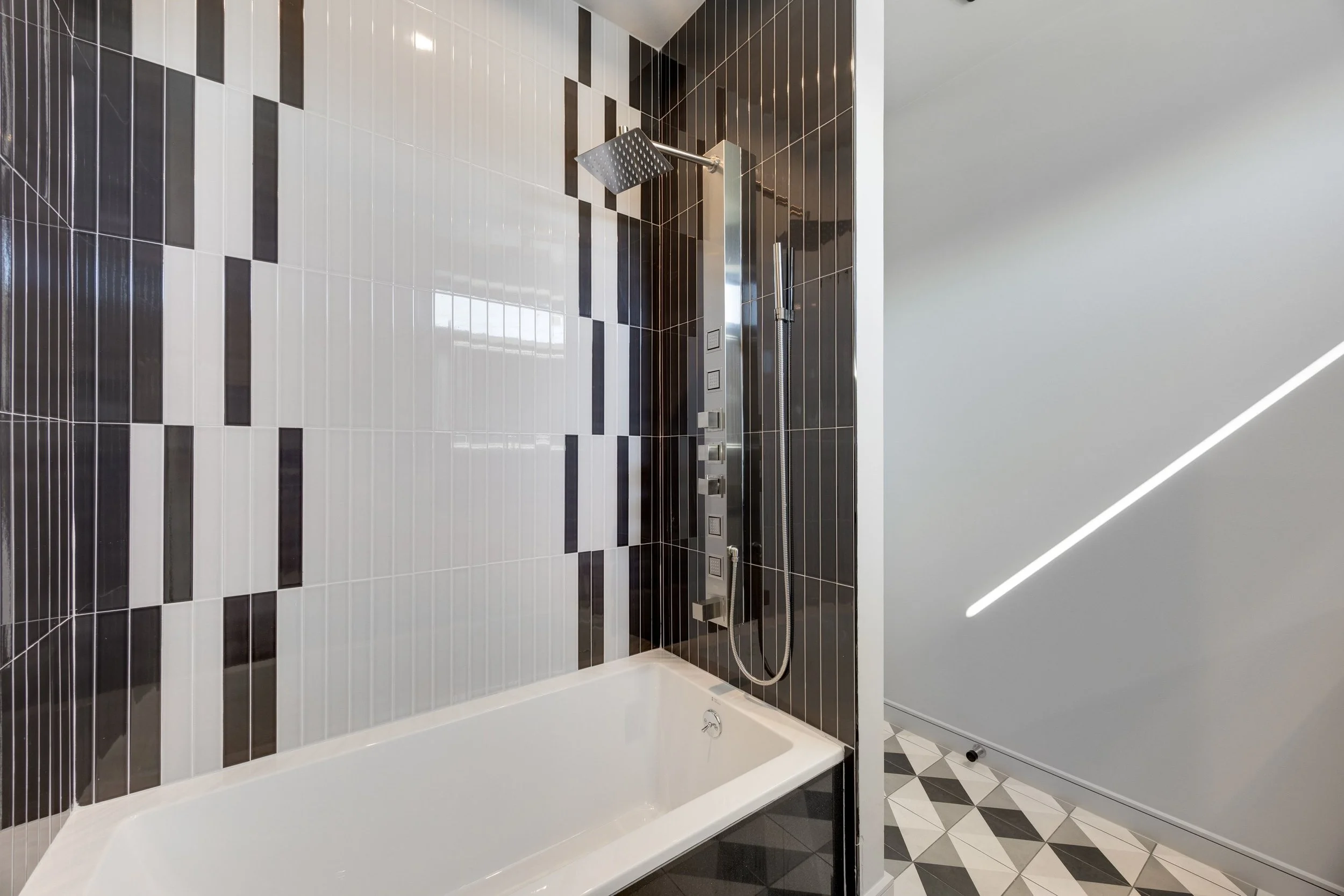 Modern bathroom shower area with black and white tiled walls, a rainfall showerhead, and a black and white patterned floor.
