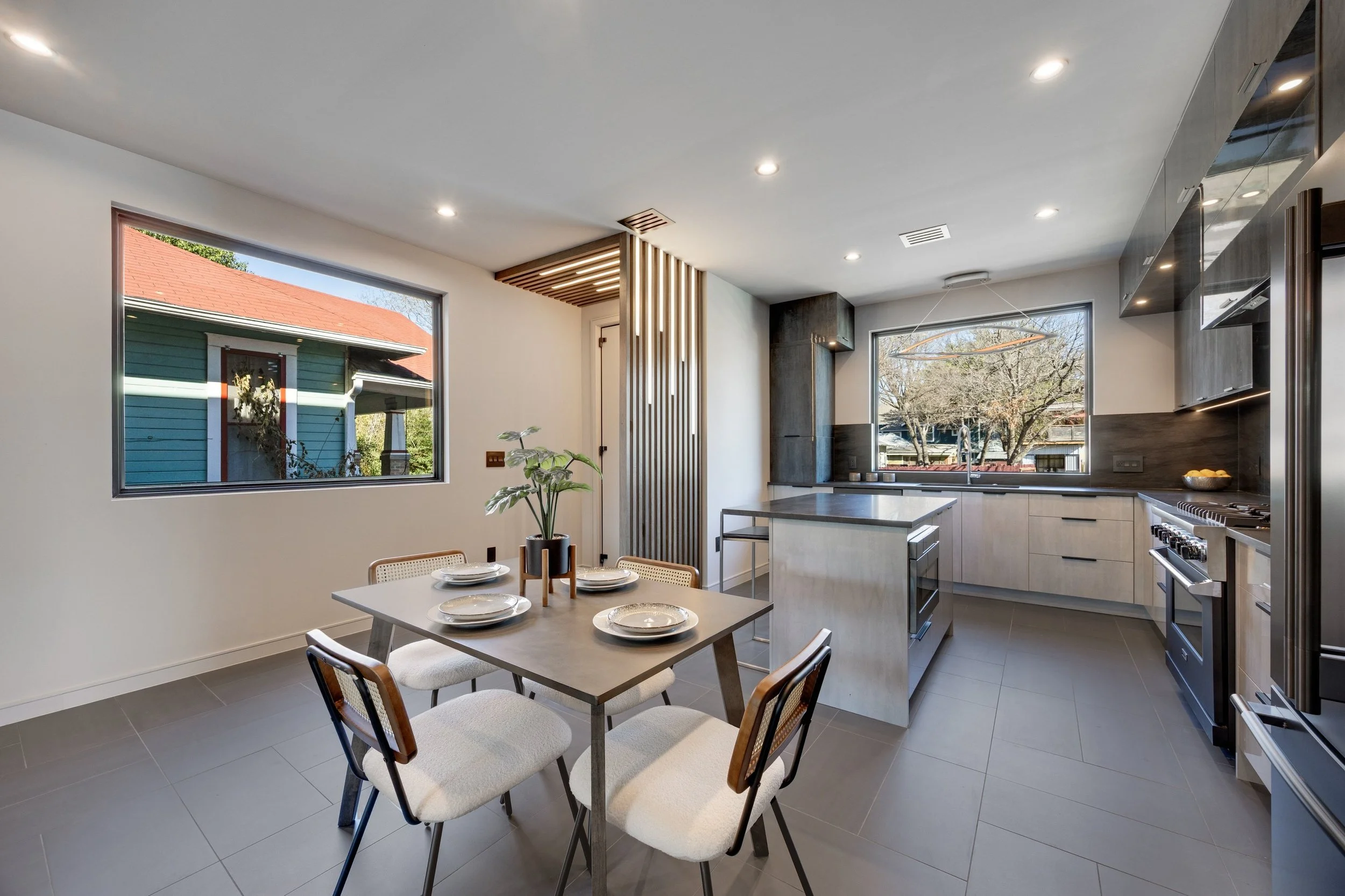 Modern kitchen with a dining table set for four, large front and side windows, and sleek cabinetry.