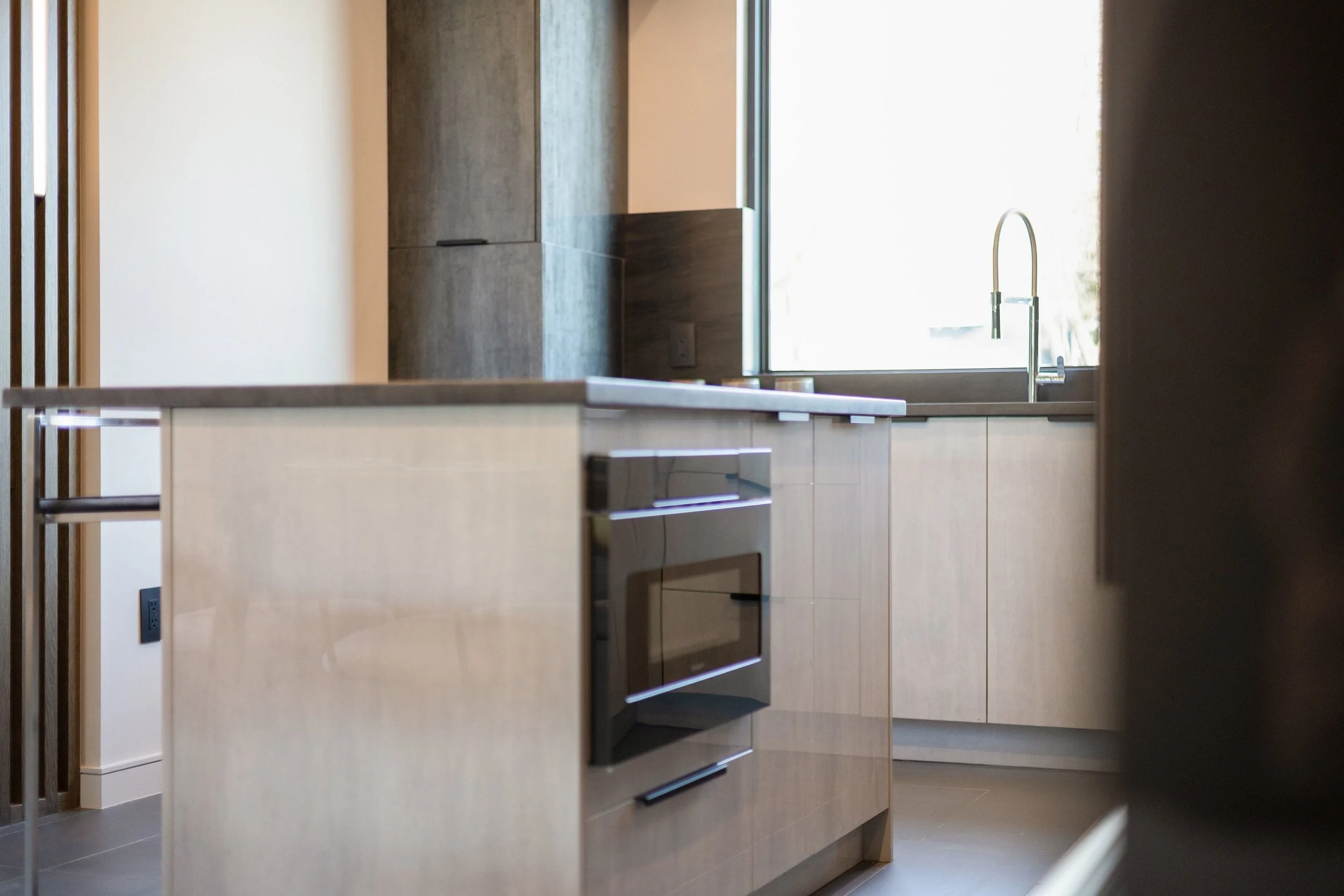 Modern kitchen with light wood cabinets, a black oven, and a large window with a sink and faucet.