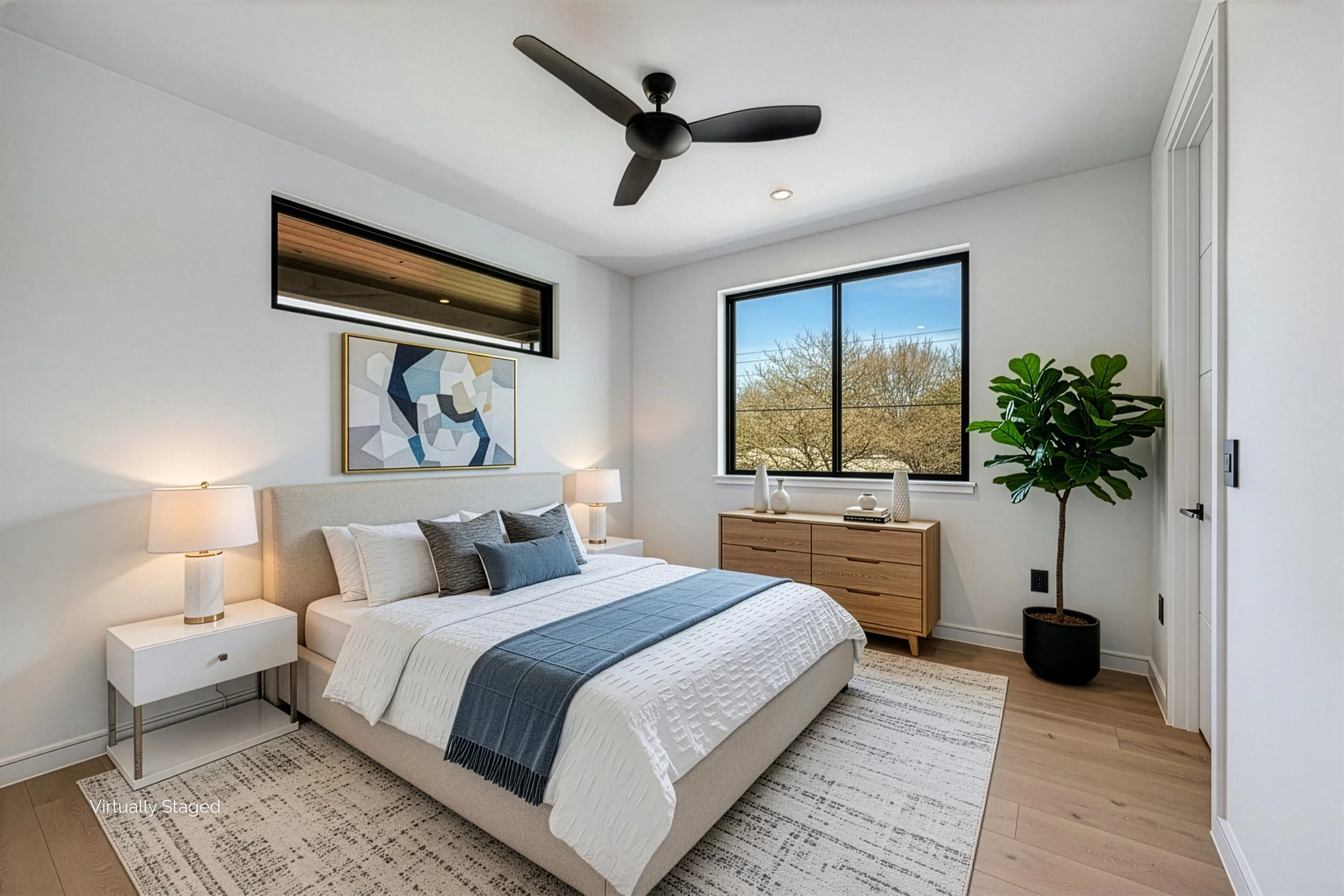 Modern bedroom with a beige bed, white and gray bedding, two nightstands with lamps, a large window showing trees, a wooden dresser with vases, a potted plant, and a ceiling fan.