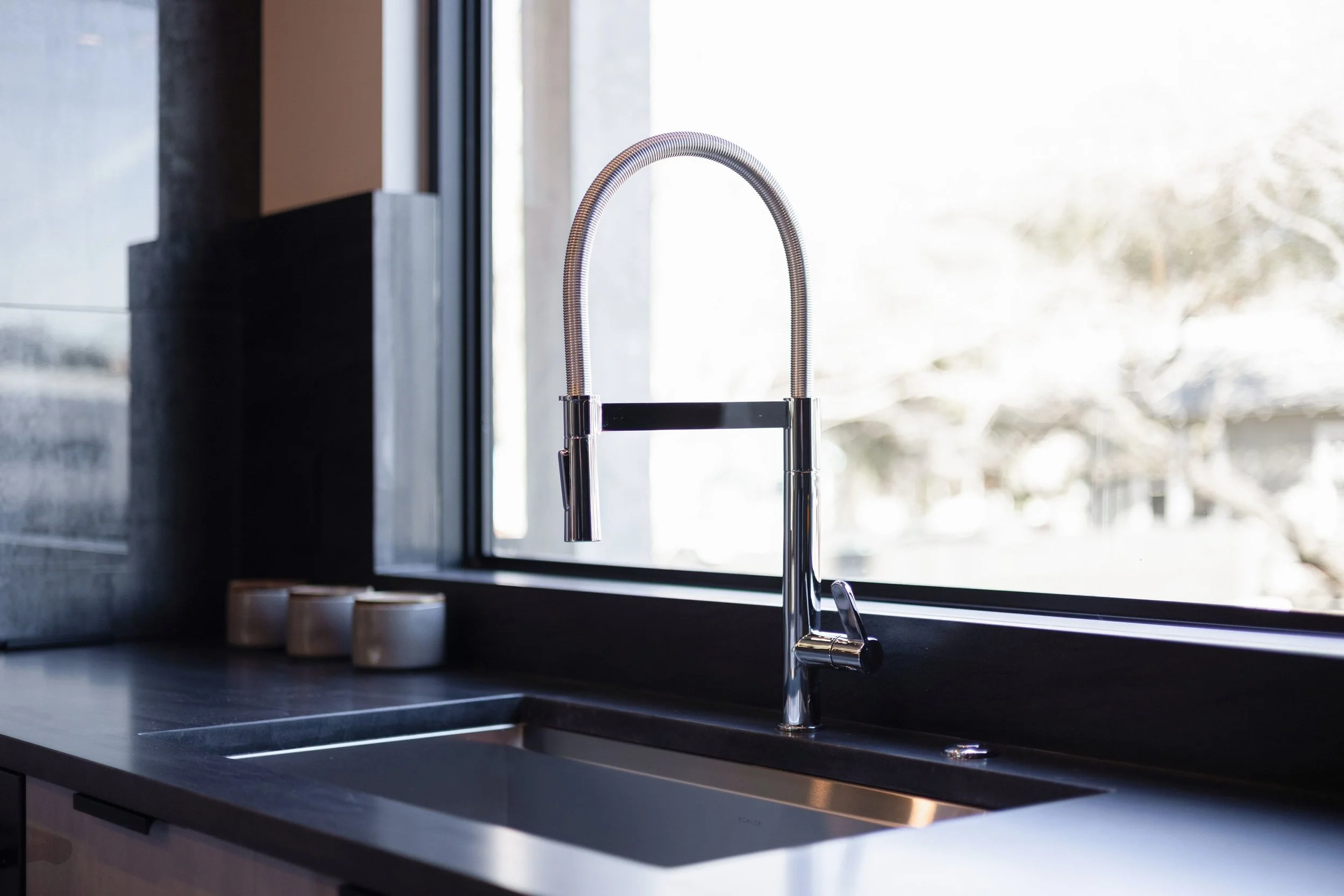A modern kitchen sink with a high-arched, flexible pull-down faucet next to a large window.
