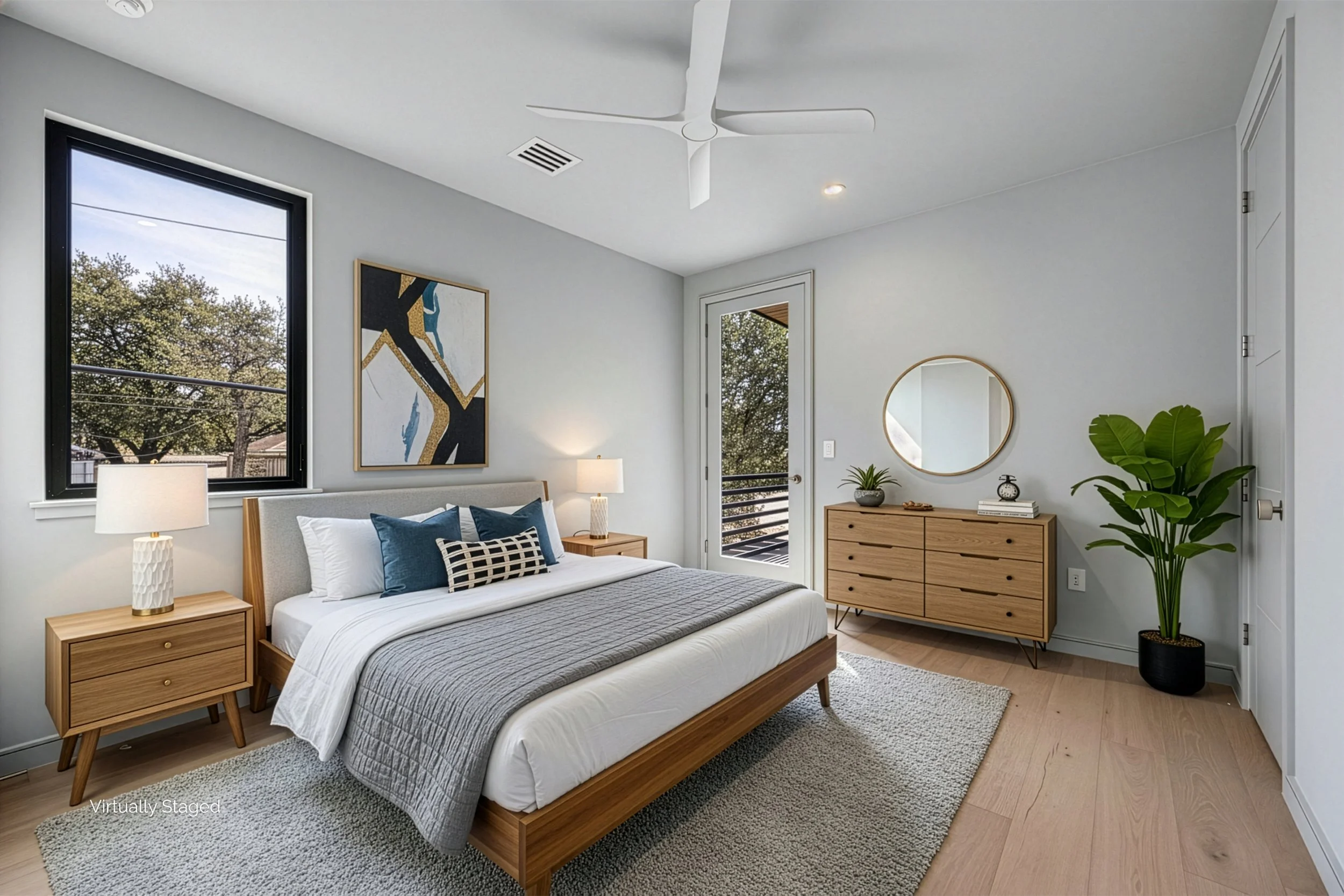 A modern bedroom with a wooden bed, white bedding, blue and black accent pillows, two wooden nightstands with lamps, a large window, a glass door leading to a balcony, a wooden dresser with a round mirror, and a large potted plant in the corner.