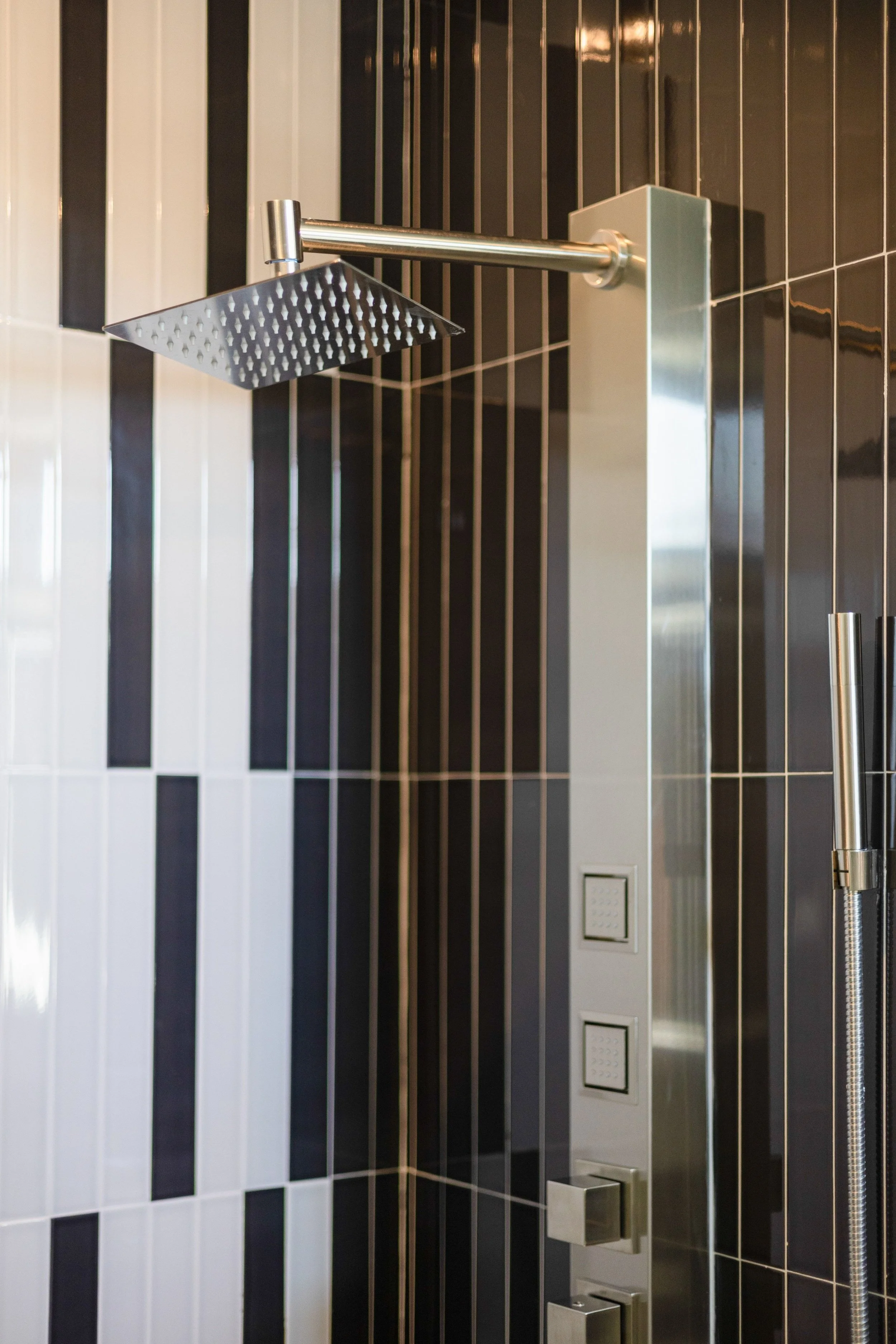 Modern shower with black and white tiled wall, rainfall showerhead, and control panels.