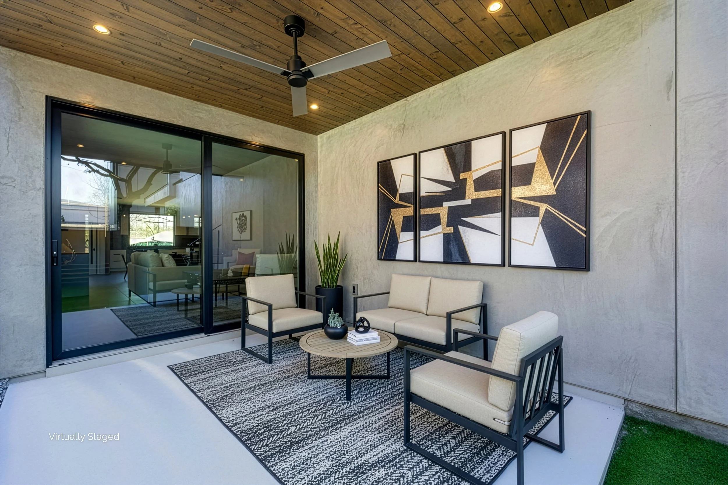 Modern patio with beige cushioned chairs and sofa, black-framed armchairs, a round wooden coffee table with decorative items, a black and white patterned rug, a tall plant in a black pot, and three large abstract artwork pieces on the wall. Sliding g