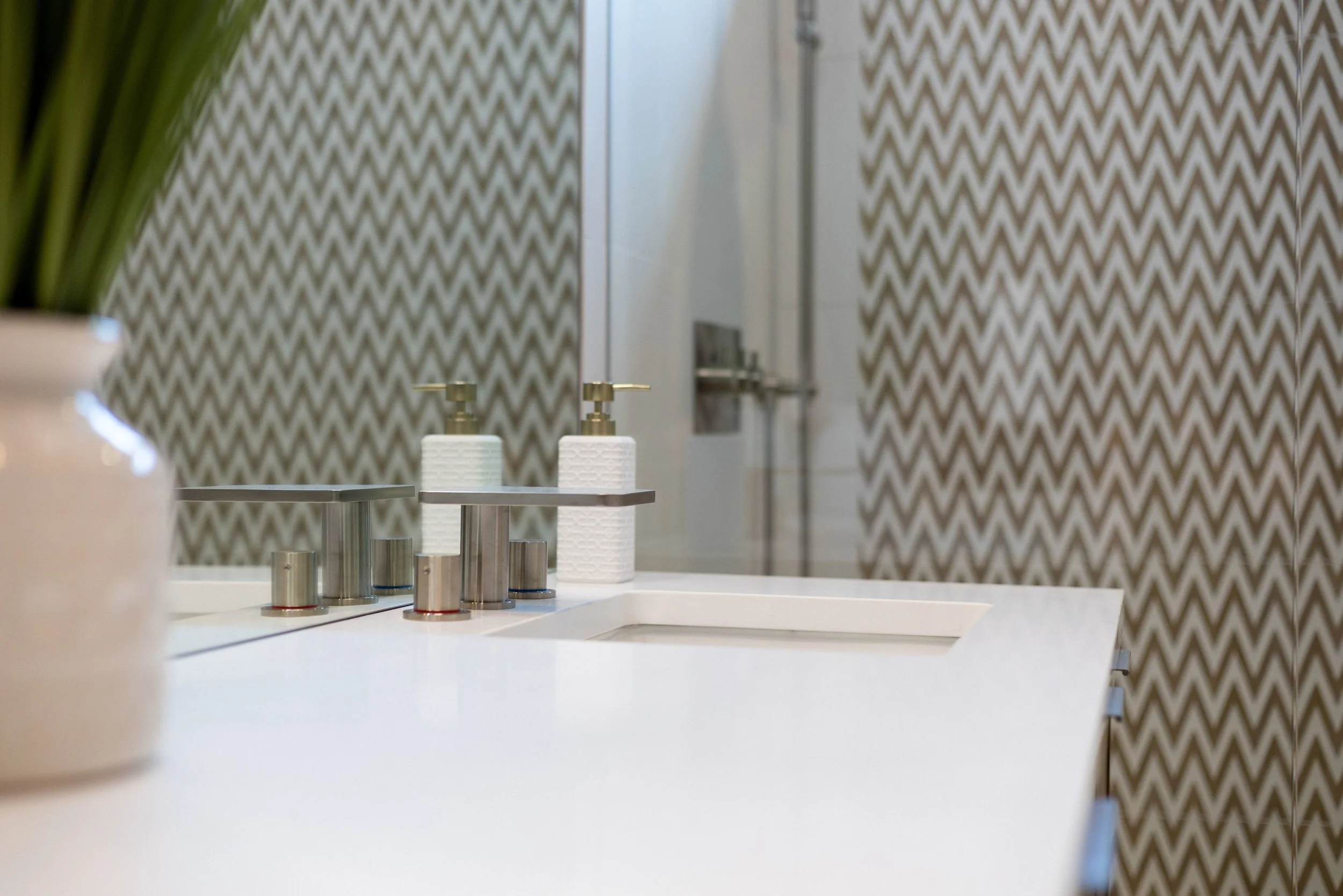Bathroom sink with soap dispensers, a mirror, and a patterned wallpaper background.