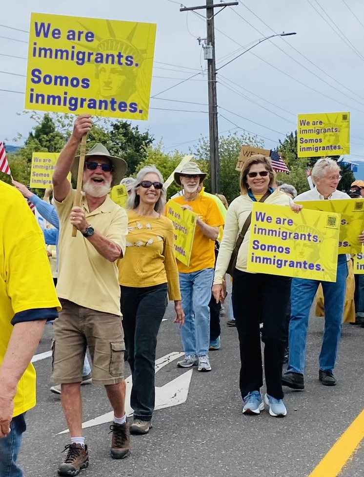 A group of people participating in a march or rally, holding yellow signs that read 'We are immigrants. Somos inmigrantes.' in both English and Spanish.