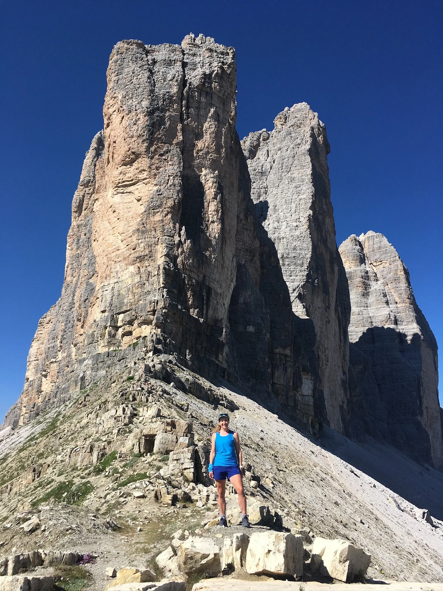 Lucy Tugwell in blue hiking gear standing in front of a large rocky mountain formation on a clear day.
