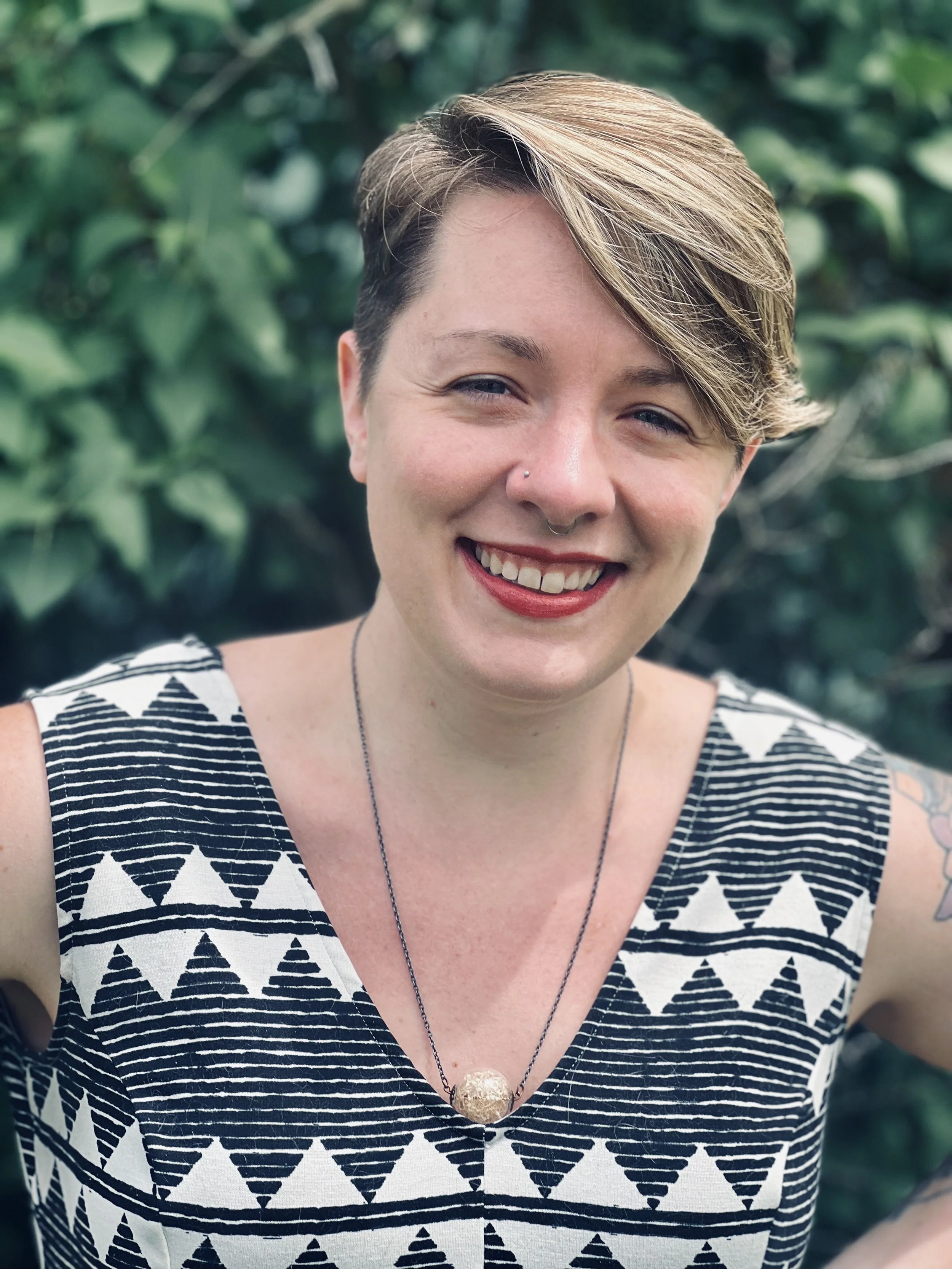 Portrait of a smiling woman with short hair and blurred green foliage in the background