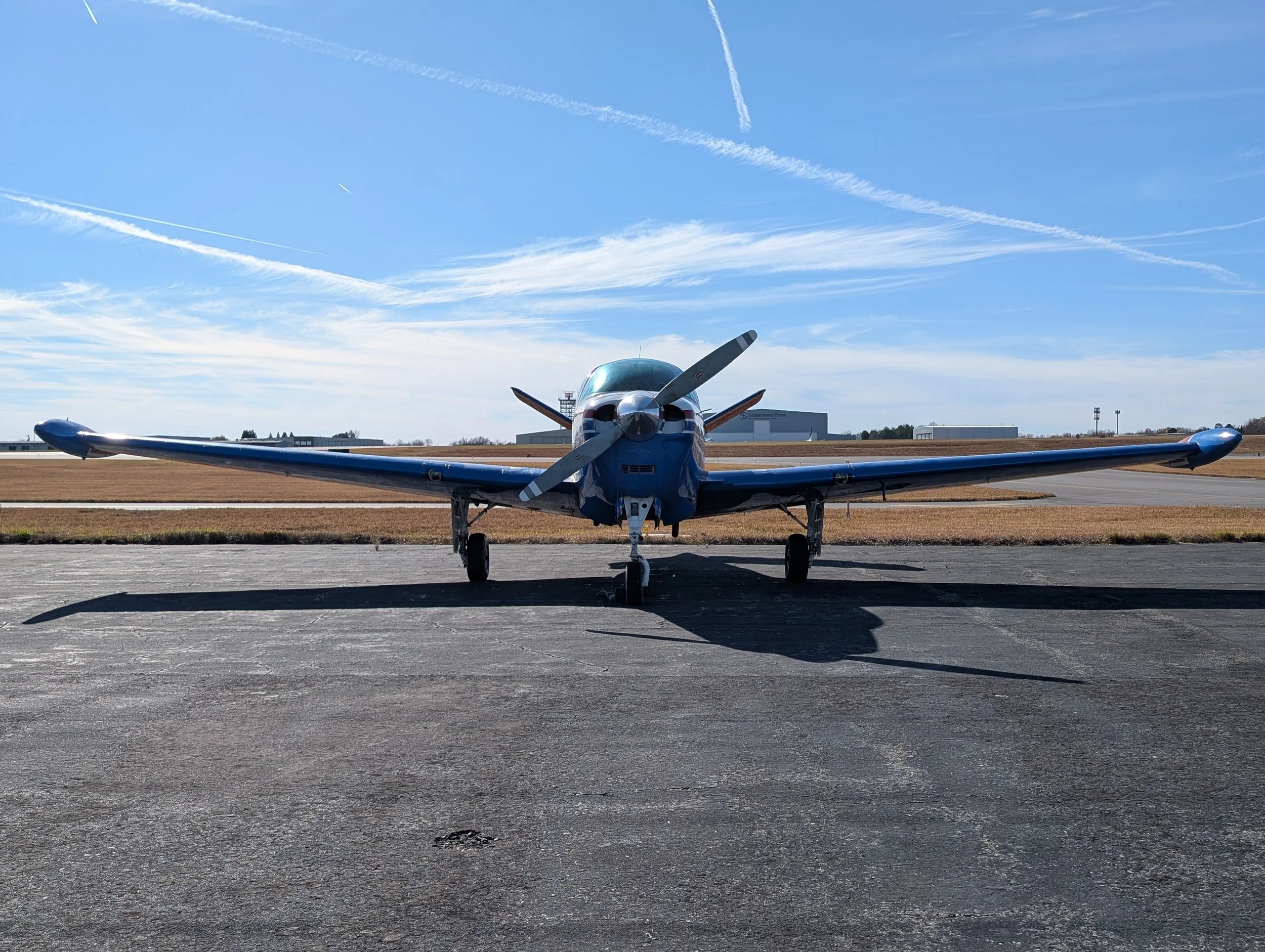 Front view of a small airplane parked on a tarmac with blue sky and wispy clouds in the background.