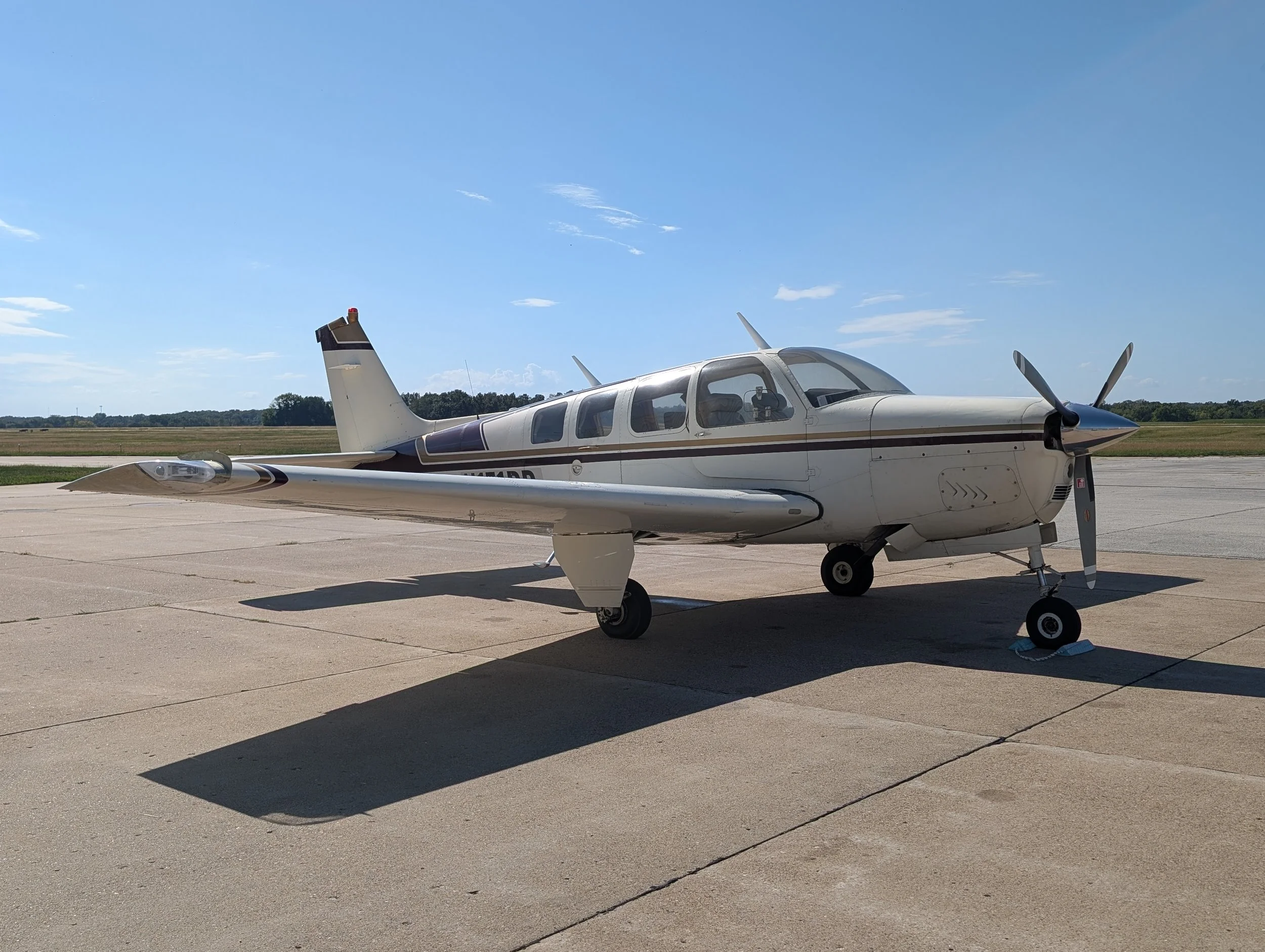 Small white private airplane parked on tarmac with a blue sky and open field in the background.