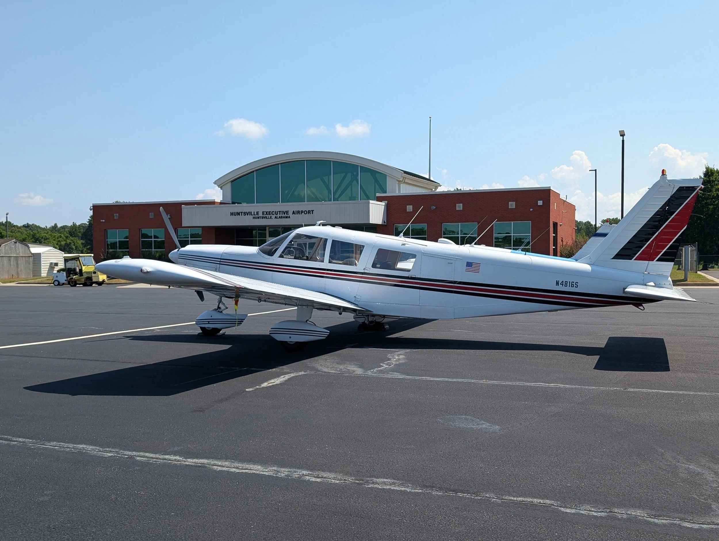 Small white private jet plane parked on the tarmac outside Huntsville Executive Airport, with a modern airport building in the background.