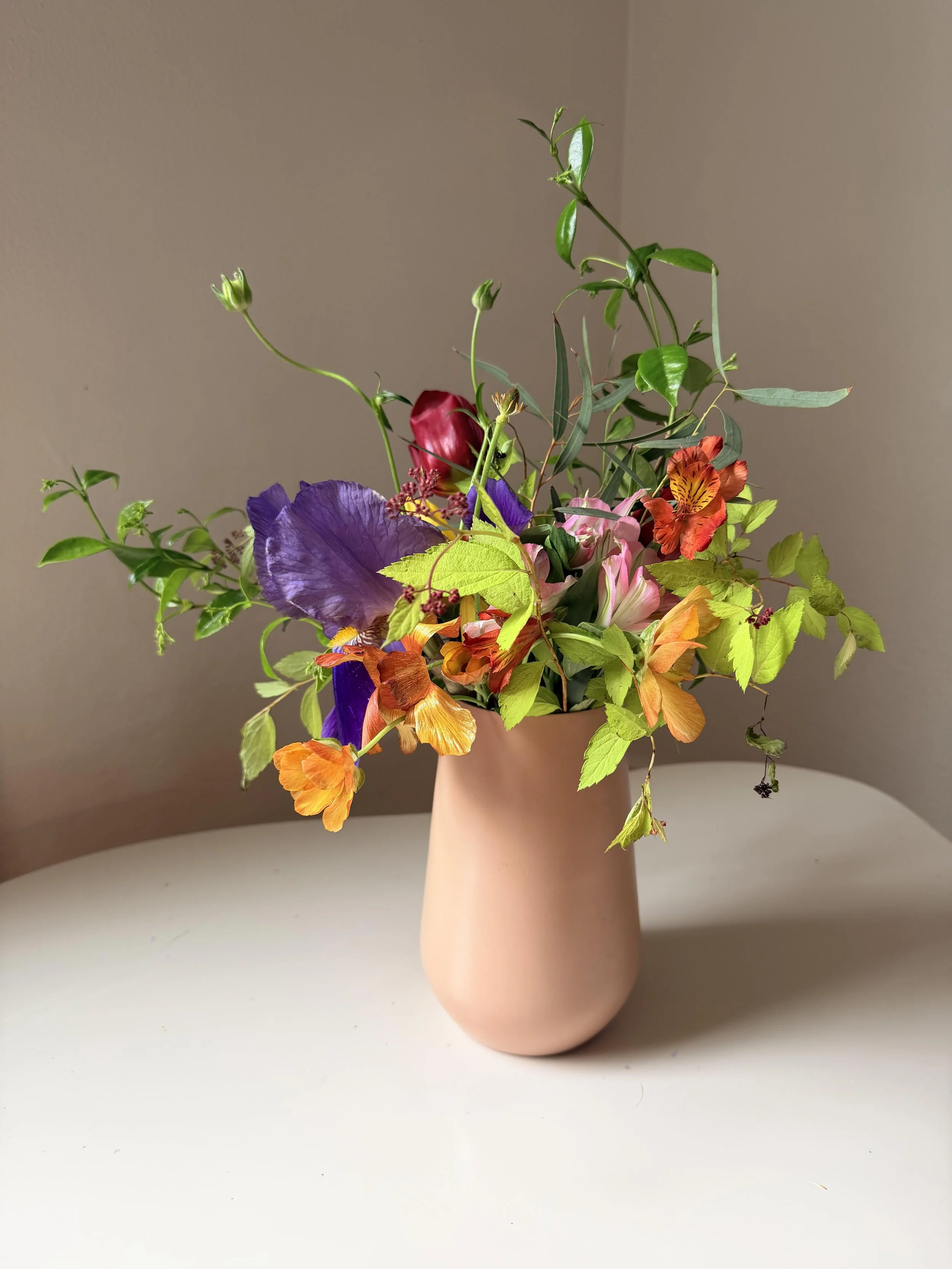 A bouquet of multicolored flowers in a pink vase on a white surface against a beige background.