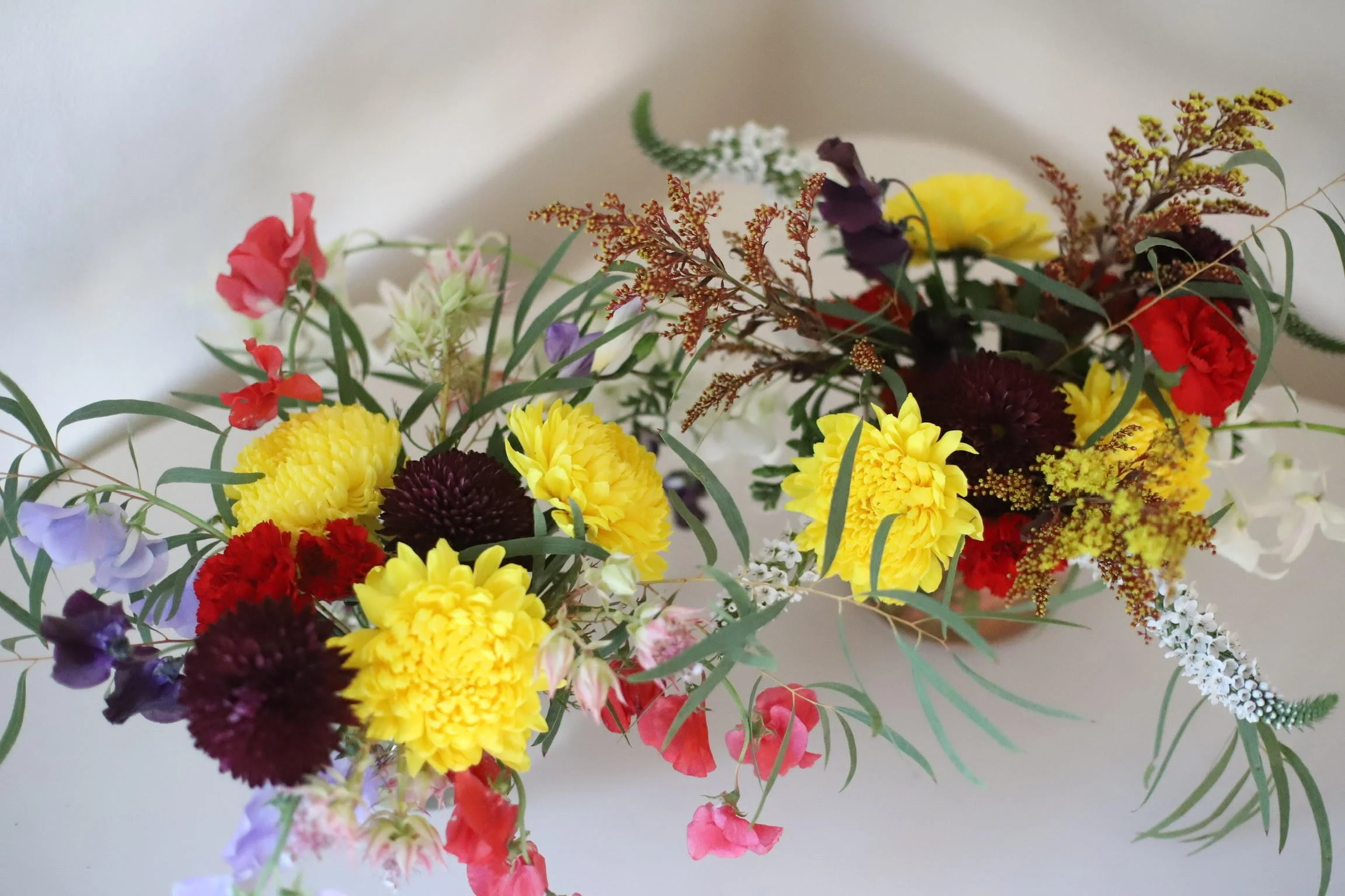 Colorful arranged bouquet of various flowers including yellow, purple, red, and white blossoms with green leaves.