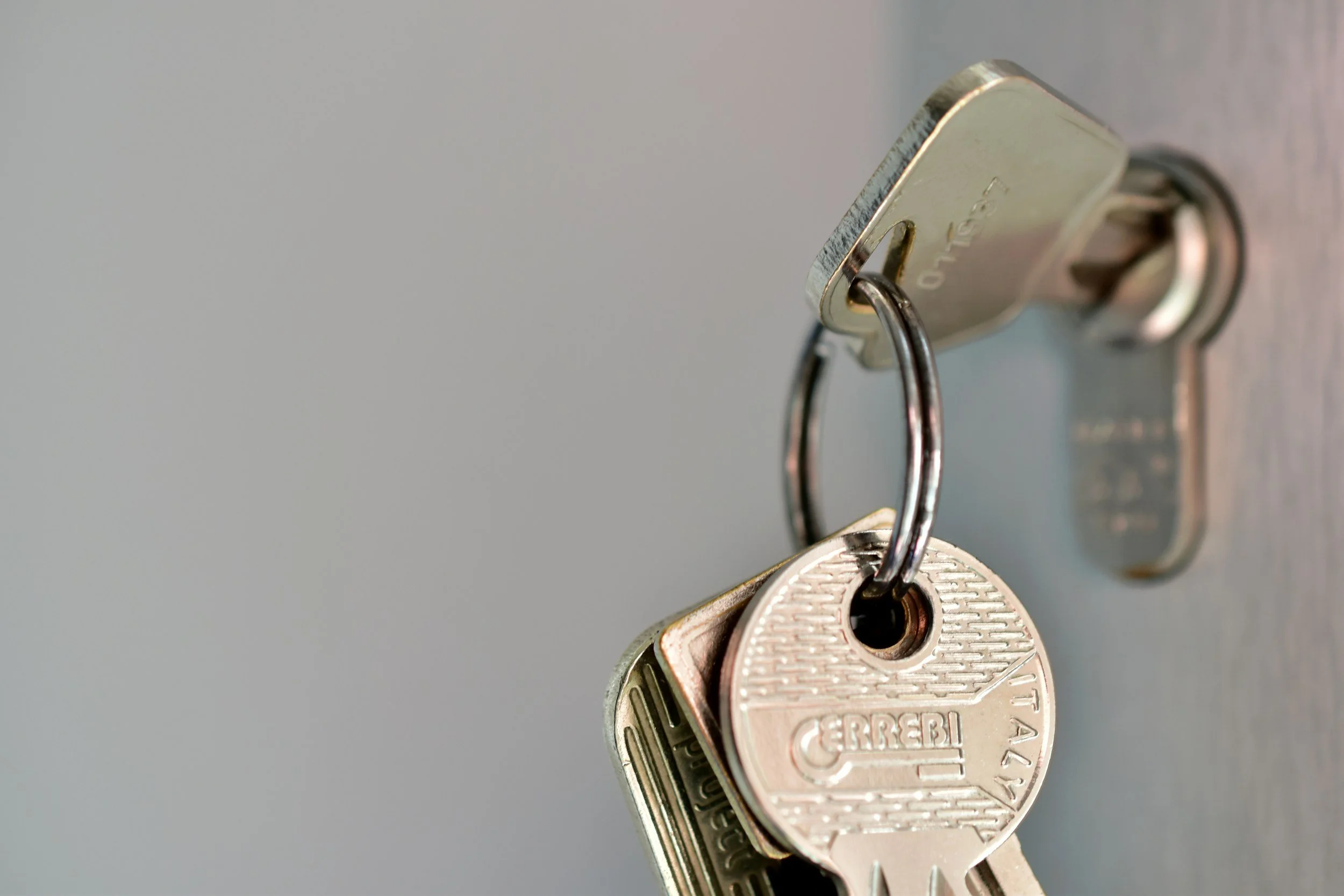 A close-up image of a set of Keys attached to a keyring with a metallic key lock in the background.