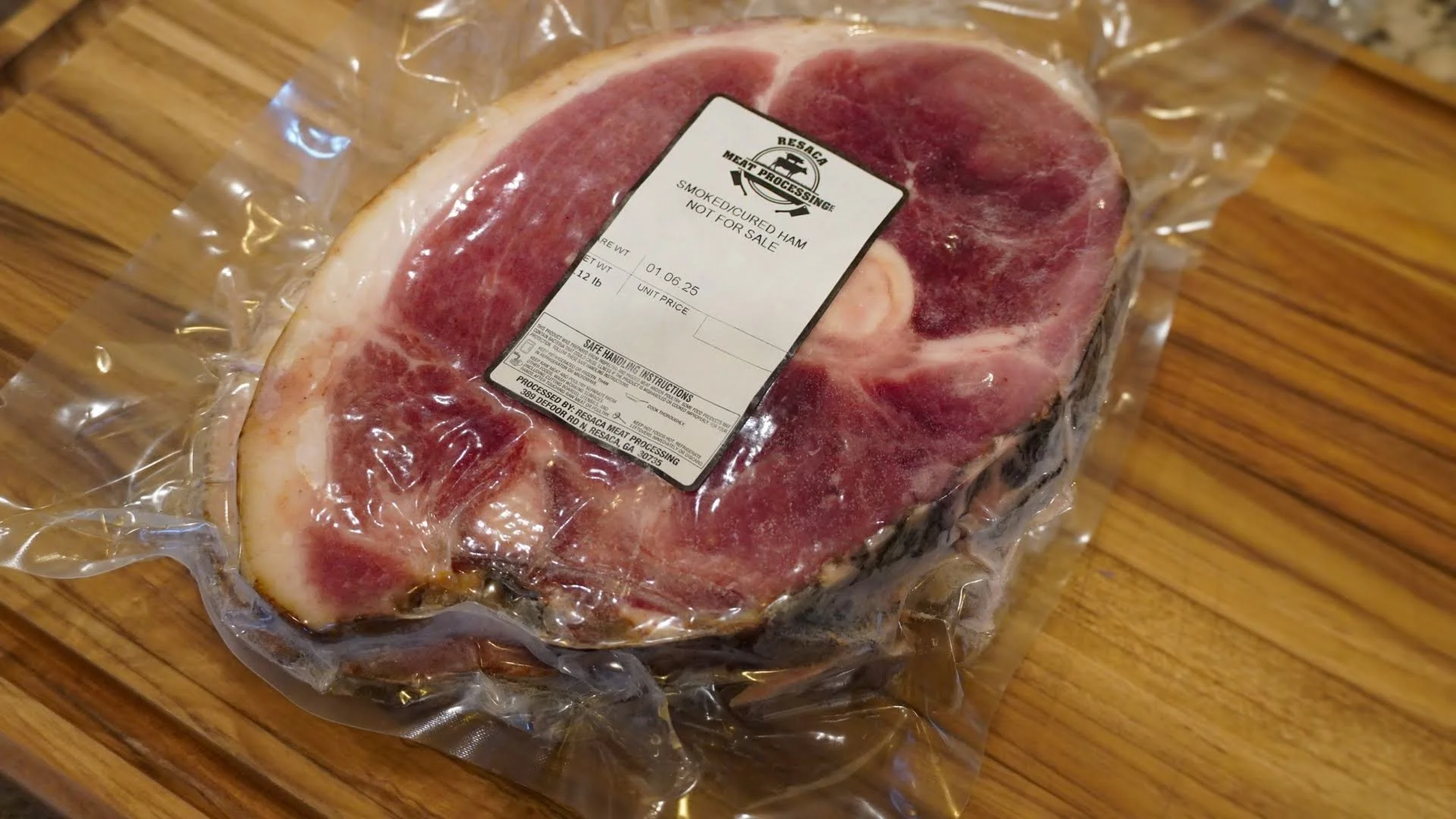 Raw smoked cured ham in vacuum-sealed packaging on a wooden surface.