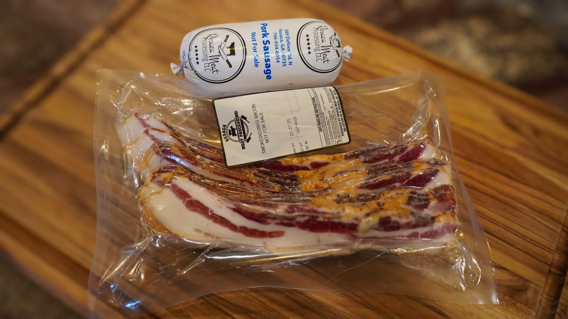 Packaged smoked bacon slices and a roll of pork sausage on a wooden surface.