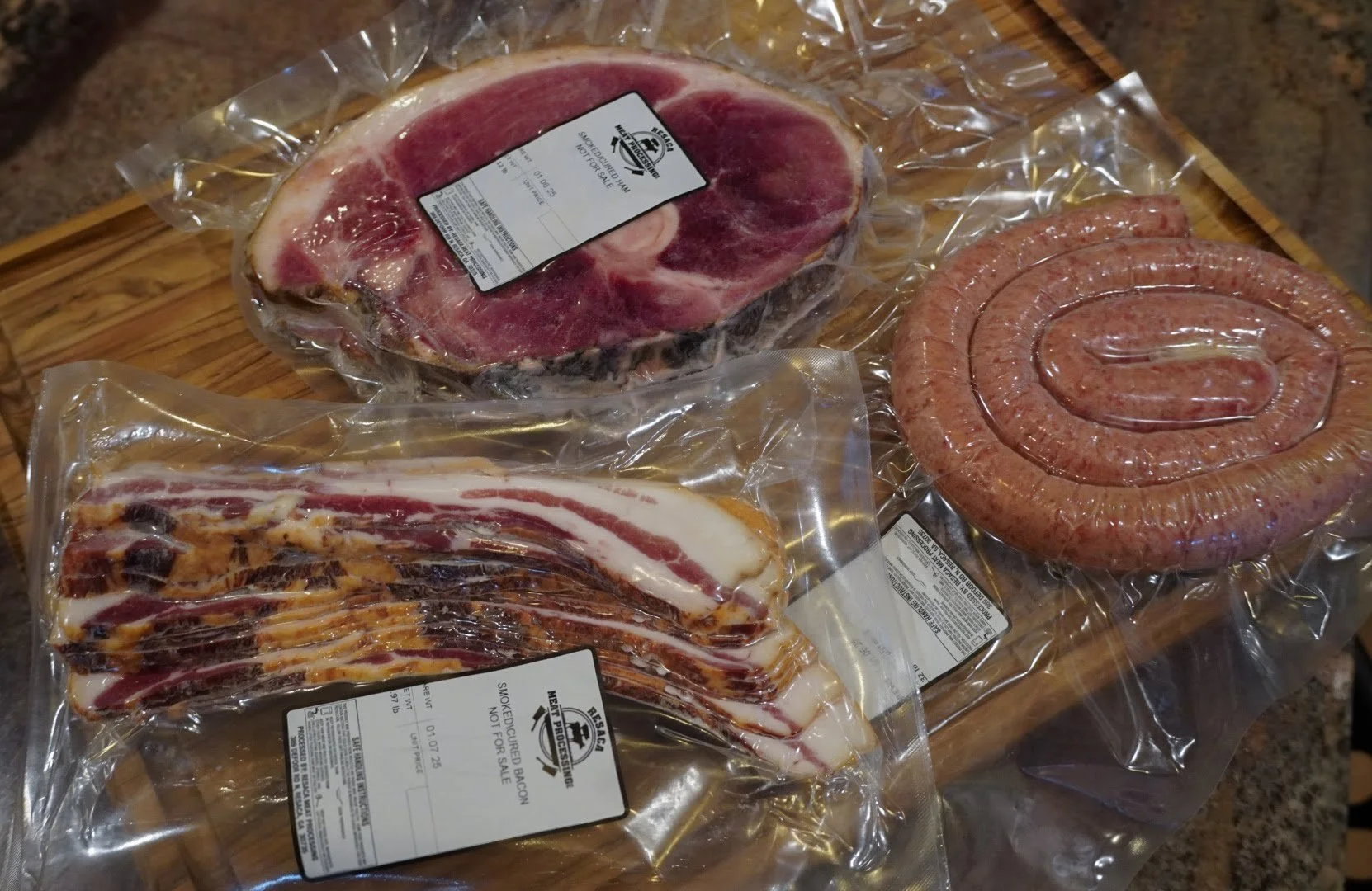 Vacuum-sealed packages of raw beef, bacon, and sausage on a wooden cutting board.
