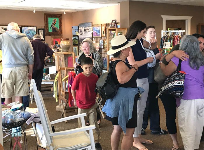 People browsing and shopping in an indoor art and craft store with paintings and decorative items displayed on walls and shelves.