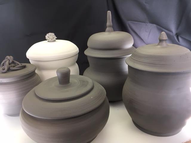 Several gray pottery urns with lids, arranged on a white surface, with a dark background.