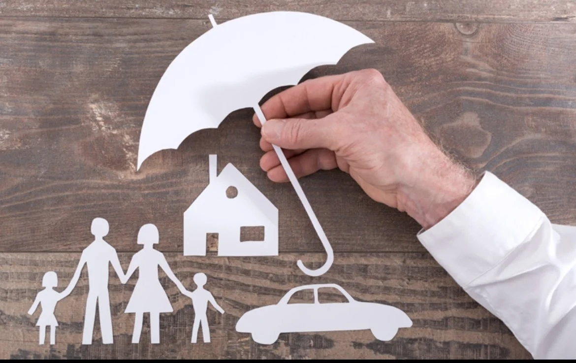 Paper cutout of a family holding hands, a house, a car, and an umbrella on a wooden surface.