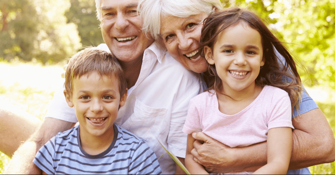 A happy multigenerational family enjoying time together outdoors on a sunny day, smiling at the camera.