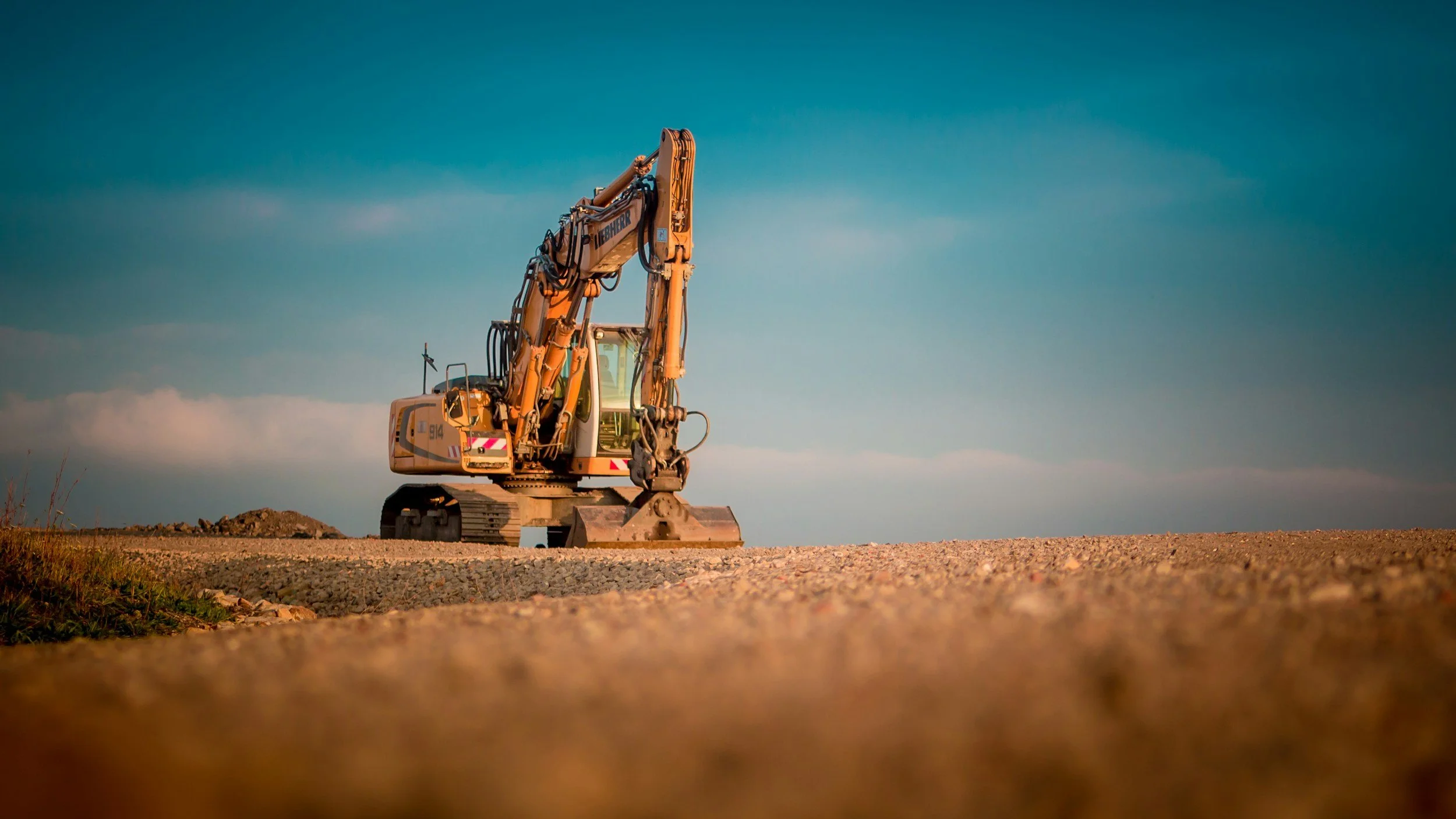 Yellow construction excavator on a dirt road under a cloudy sky.